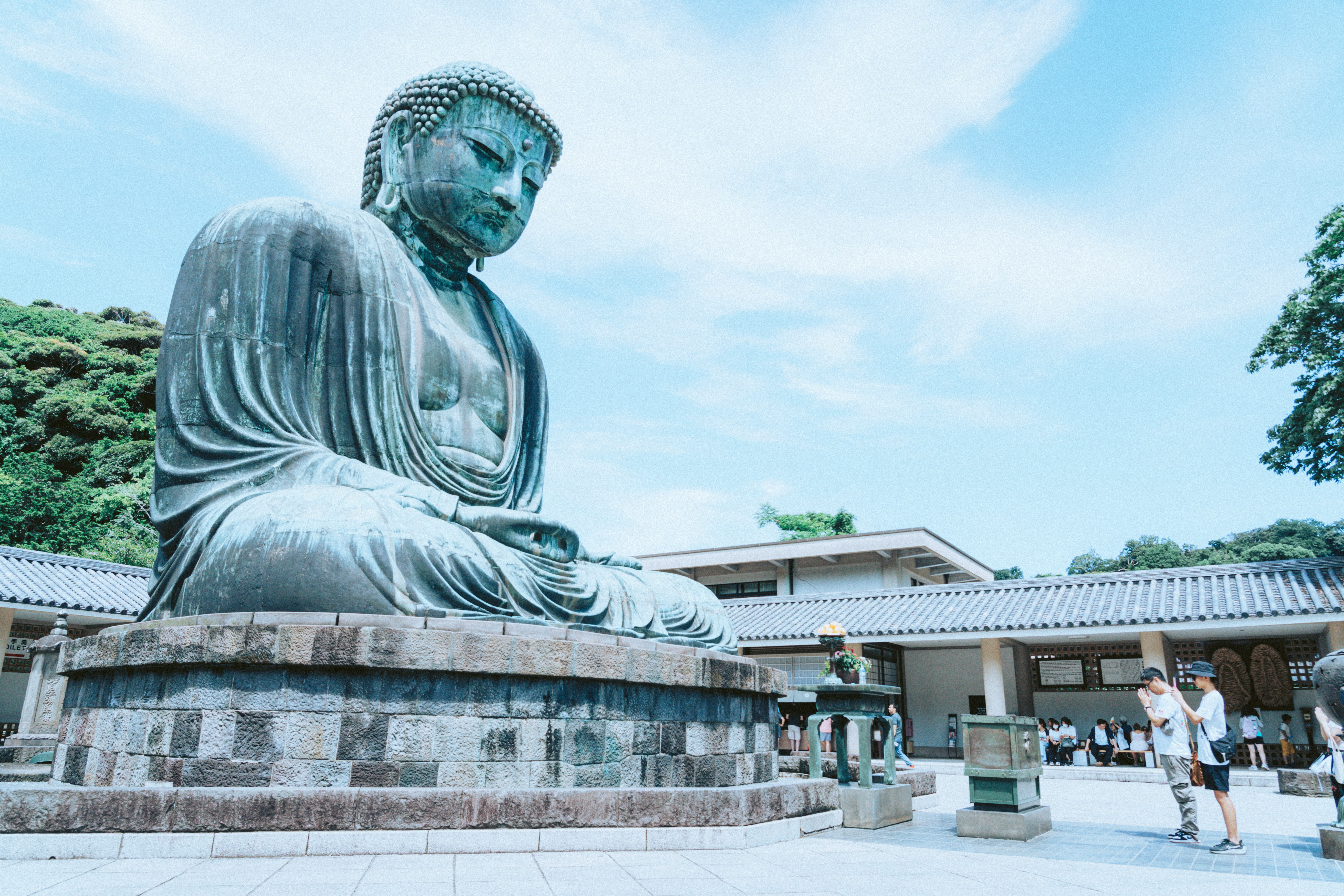 outdoor temple courtyard with a large bronze Buddha statue on a stone pedestal