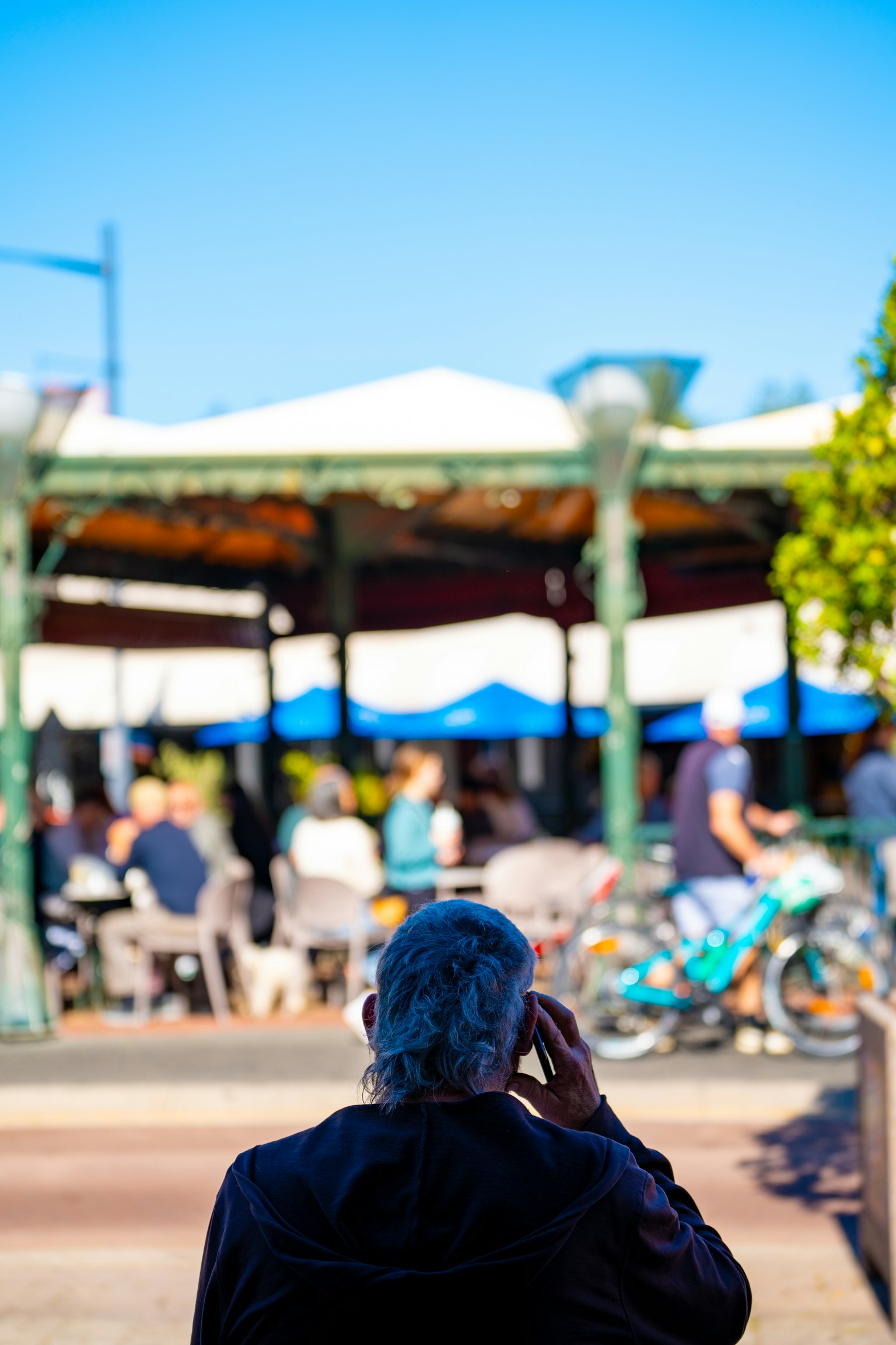 Mann am Telefon mit Café im Freien im Hintergrund, das einen blauen Himmel und Tische zeigt
