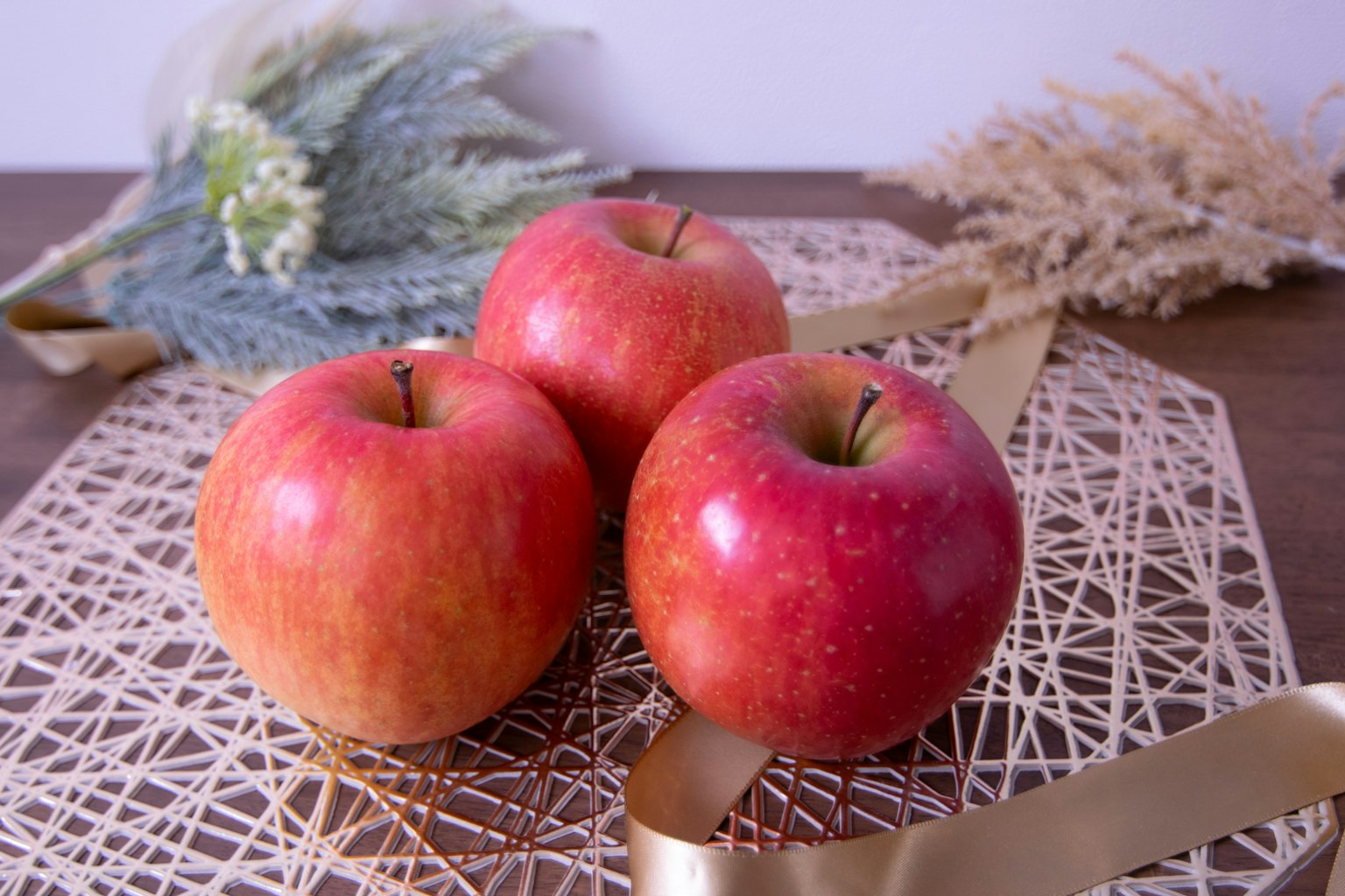 Tres manzanas rojas dispuestas sobre una superficie decorativa con flores secas