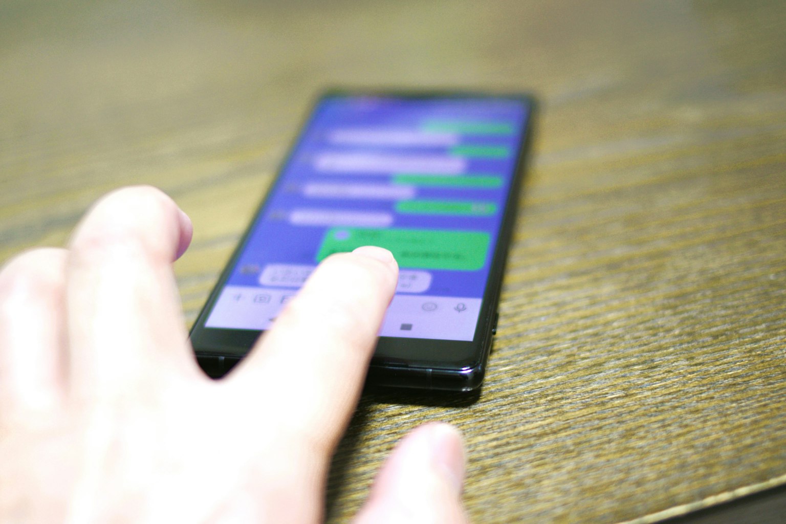 Ein Smartphone auf einem Holztisch mit einem Finger, der den Bildschirm der Messaging-App berührt