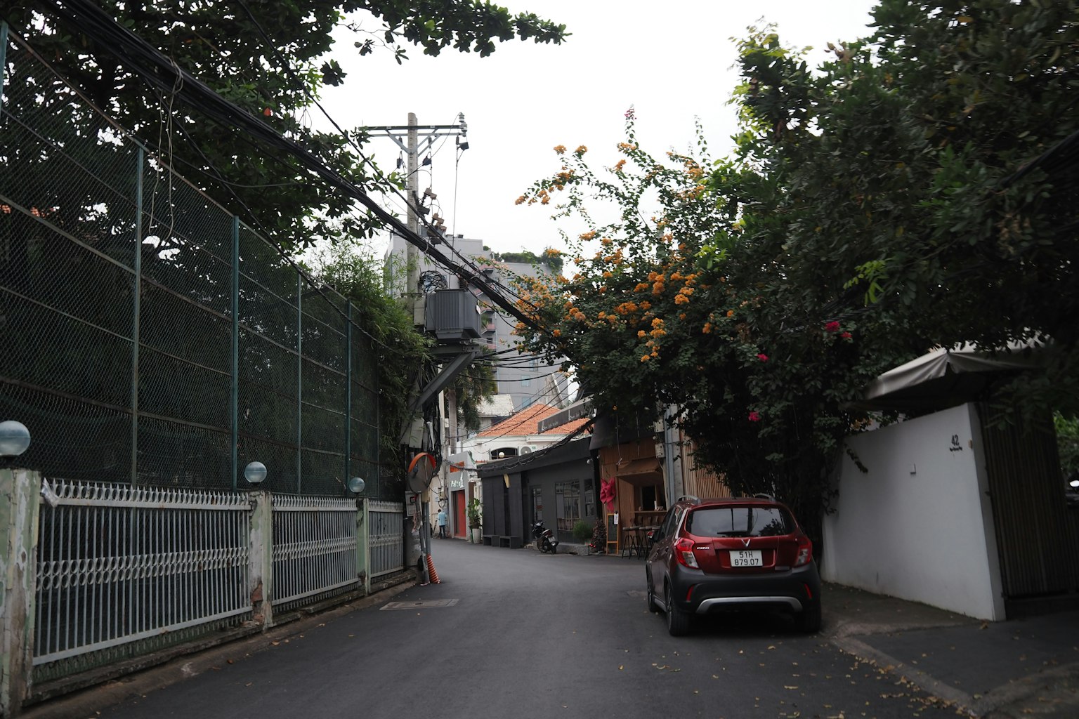 Strada stretta in un'area residenziale con un'auto rossa parcheggiata e alberi verdi lussureggianti