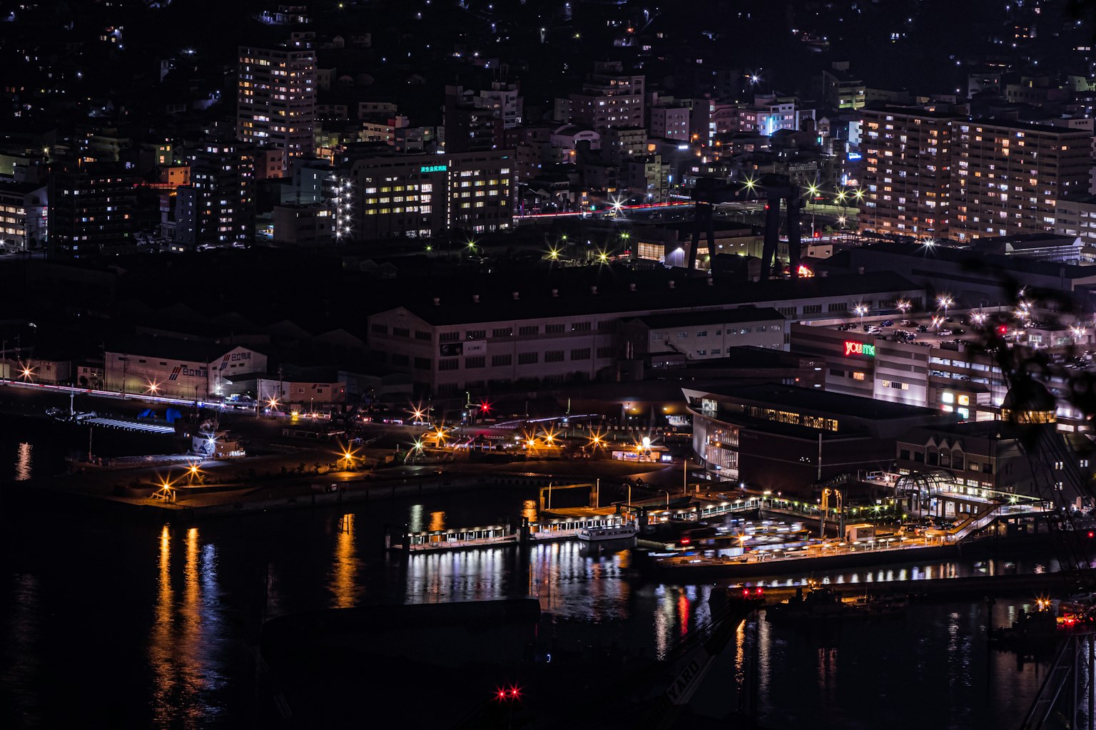 Belle vue nocturne d'une ville portuaire avec des bâtiments illuminés et des bateaux se reflétant sur l'eau