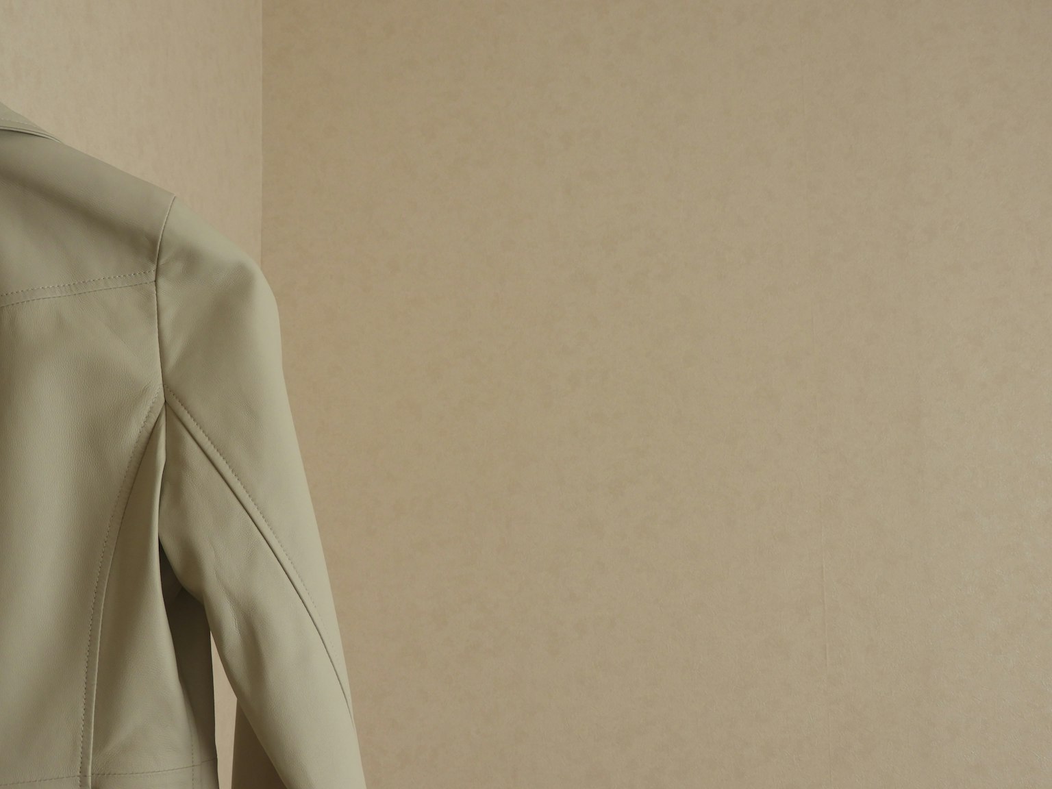 Part of a light-colored jacket against a beige wall