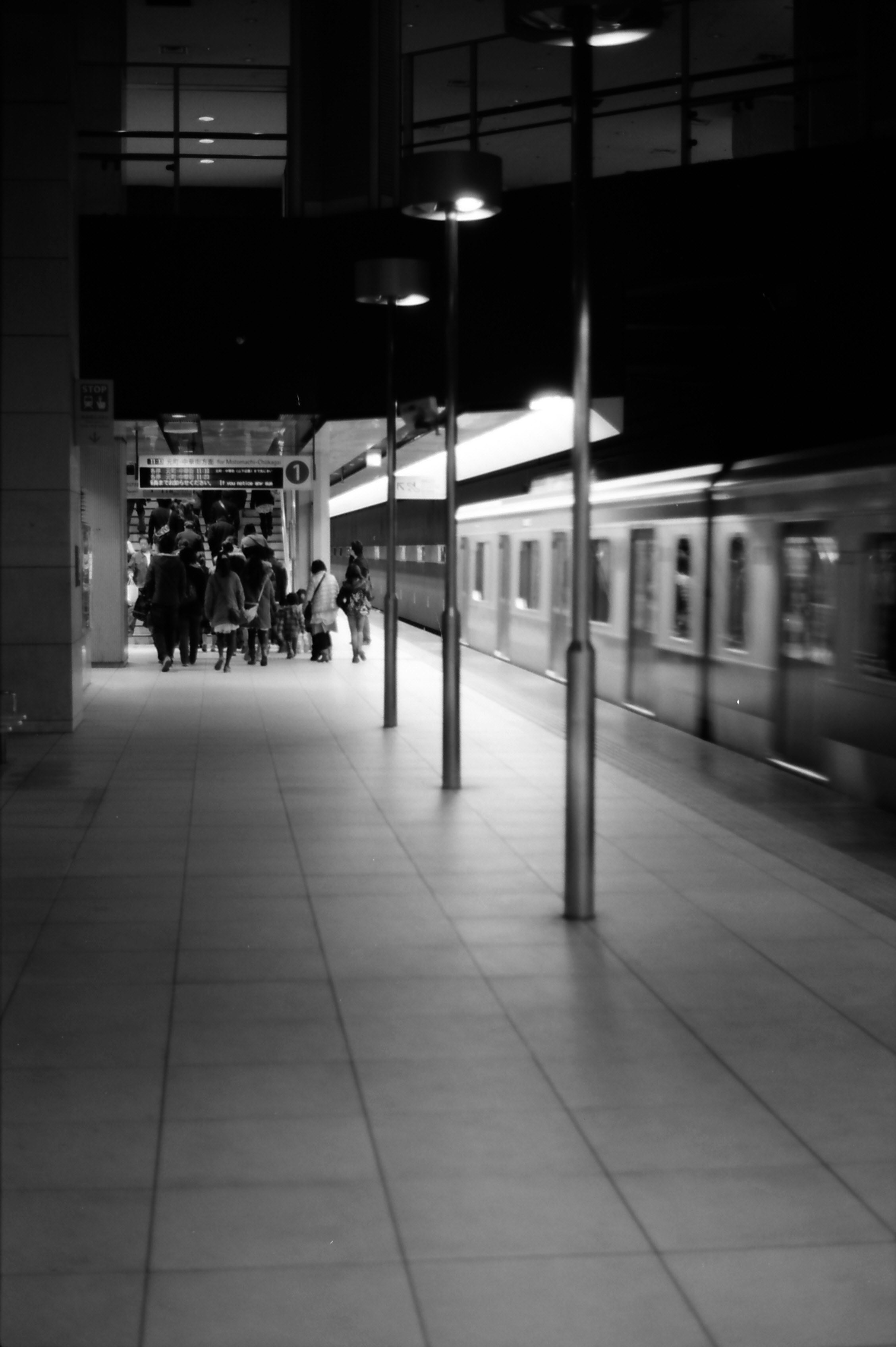 横浜の夜の駅構内で電車が通り過ぎるホームのモノクロ風景