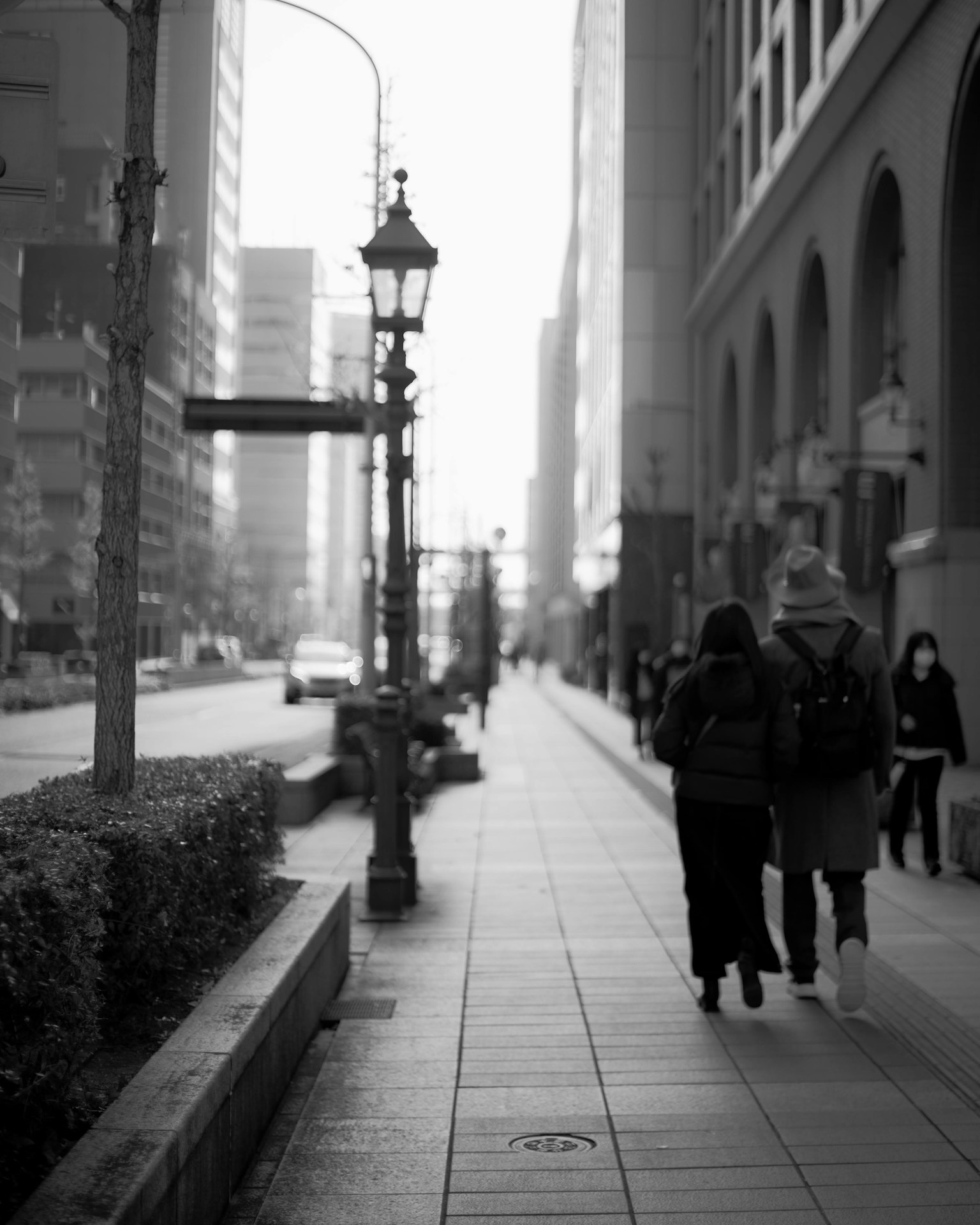 Black and white urban scene featuring two people walking on a sidewalk with a street lamp