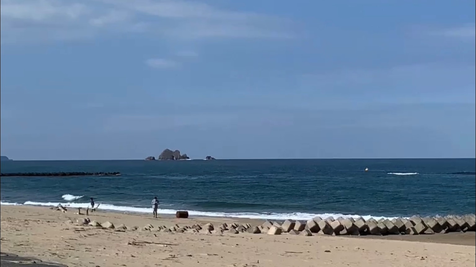 Scenic view of blue ocean and sandy beach with people walking