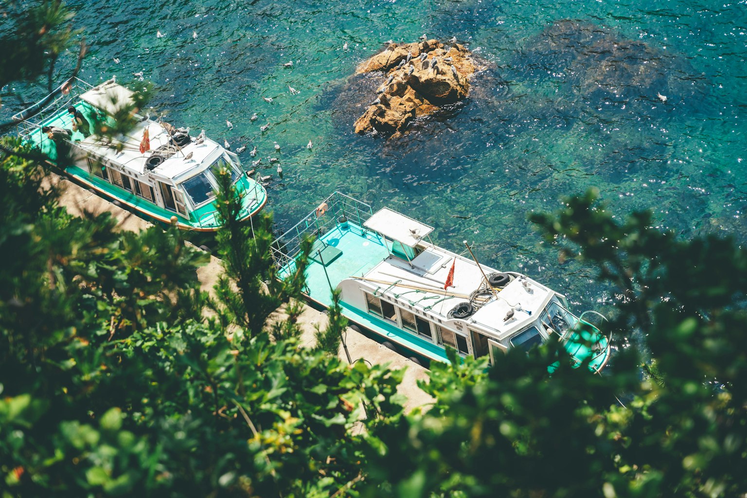 Deux bateaux amarrés près d'une mer bleue avec un rocher