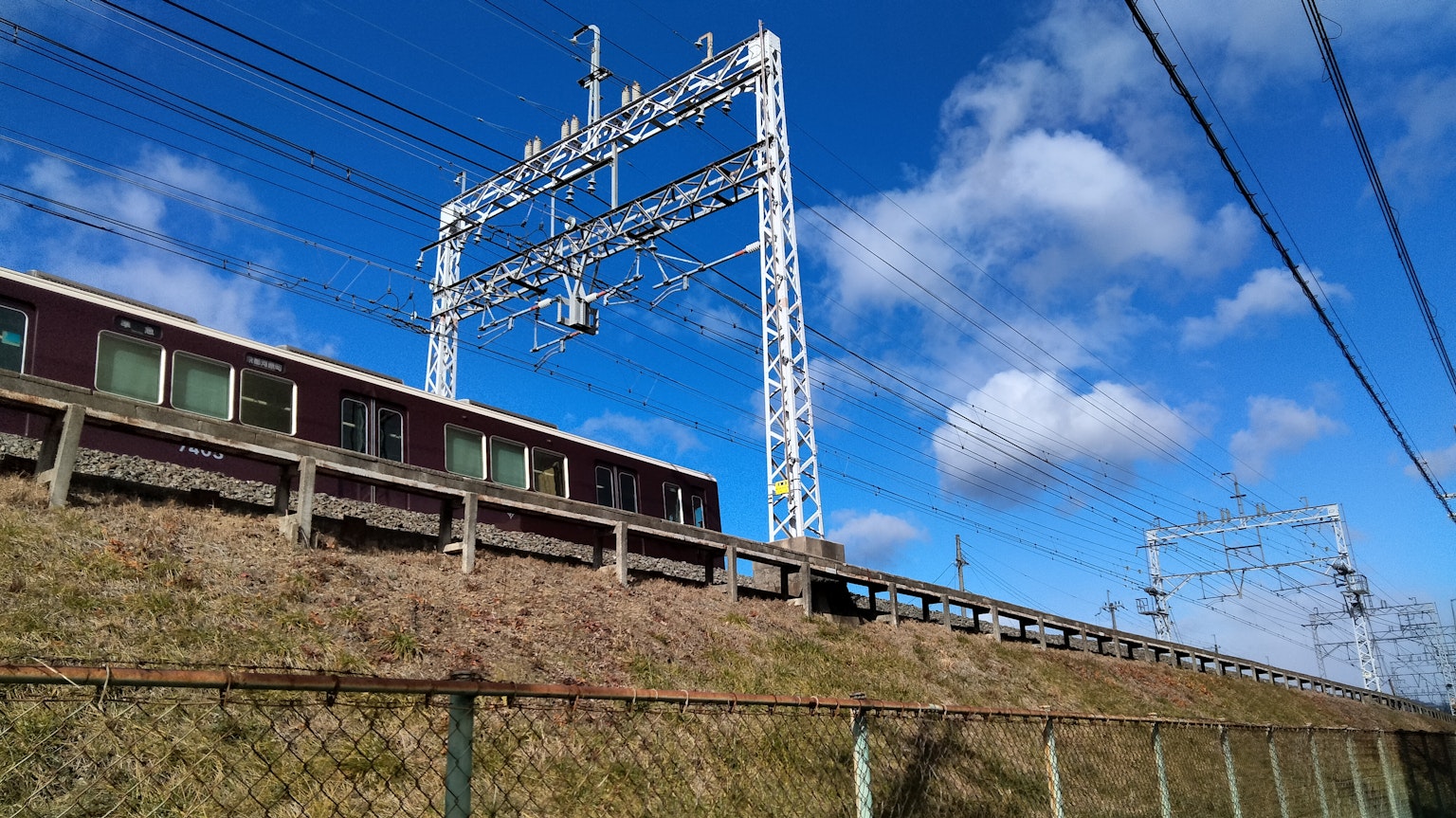 Treno ferroviario e linee aeree sotto un cielo blu con nuvole