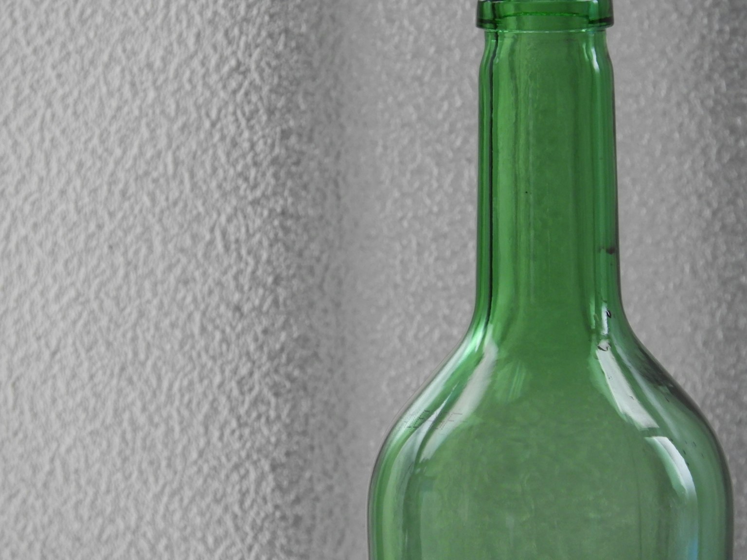 Une bouteille en verre verte sur un fond texturé blanc