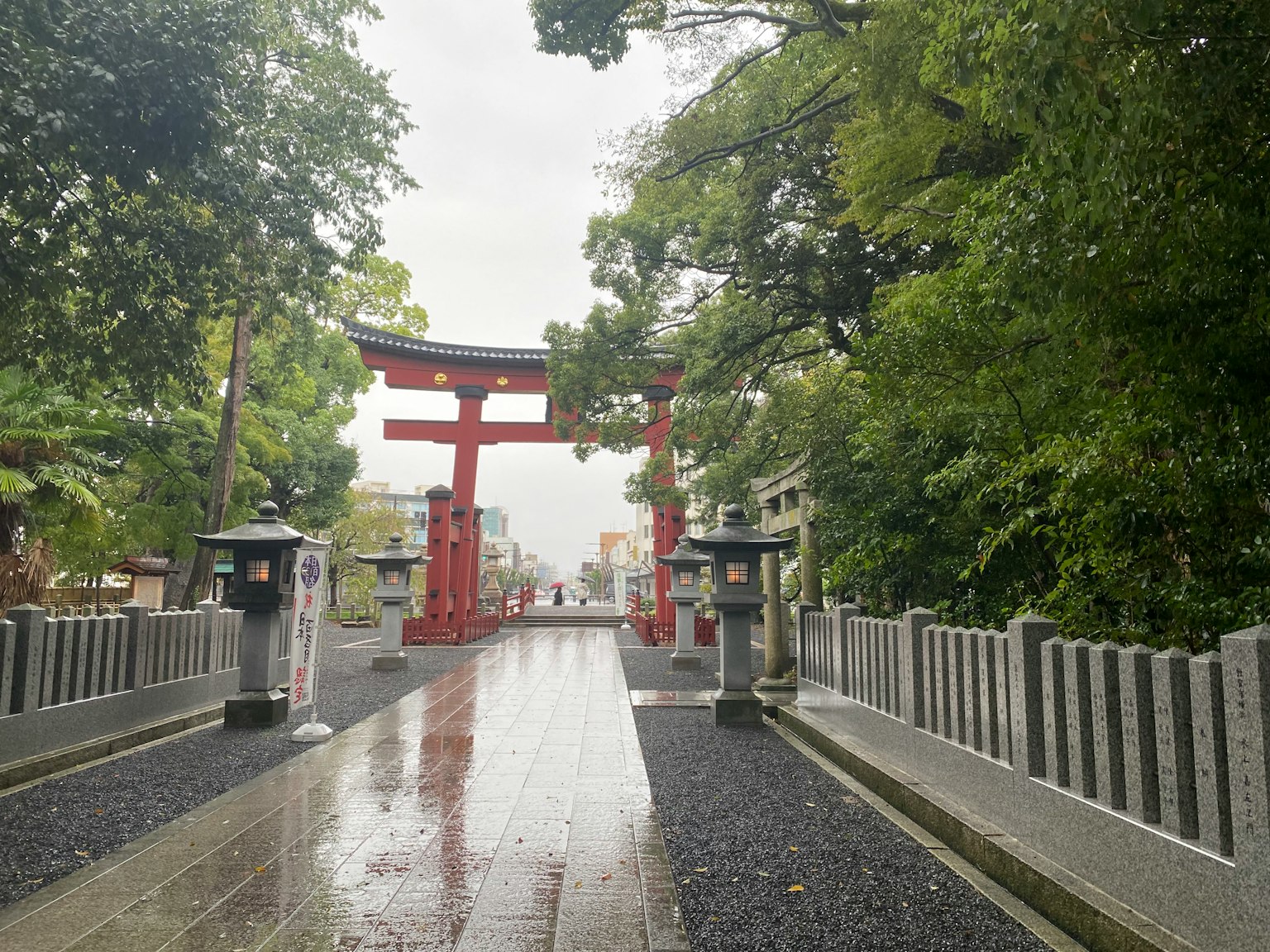 Pathway leading to a shrine with a red torii gate and stone lanterns wet pavement and lush greenery