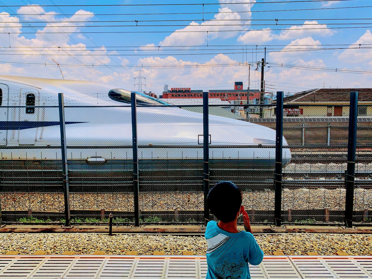 Child watching a Shinkansen train with blue sky and clouds in the background