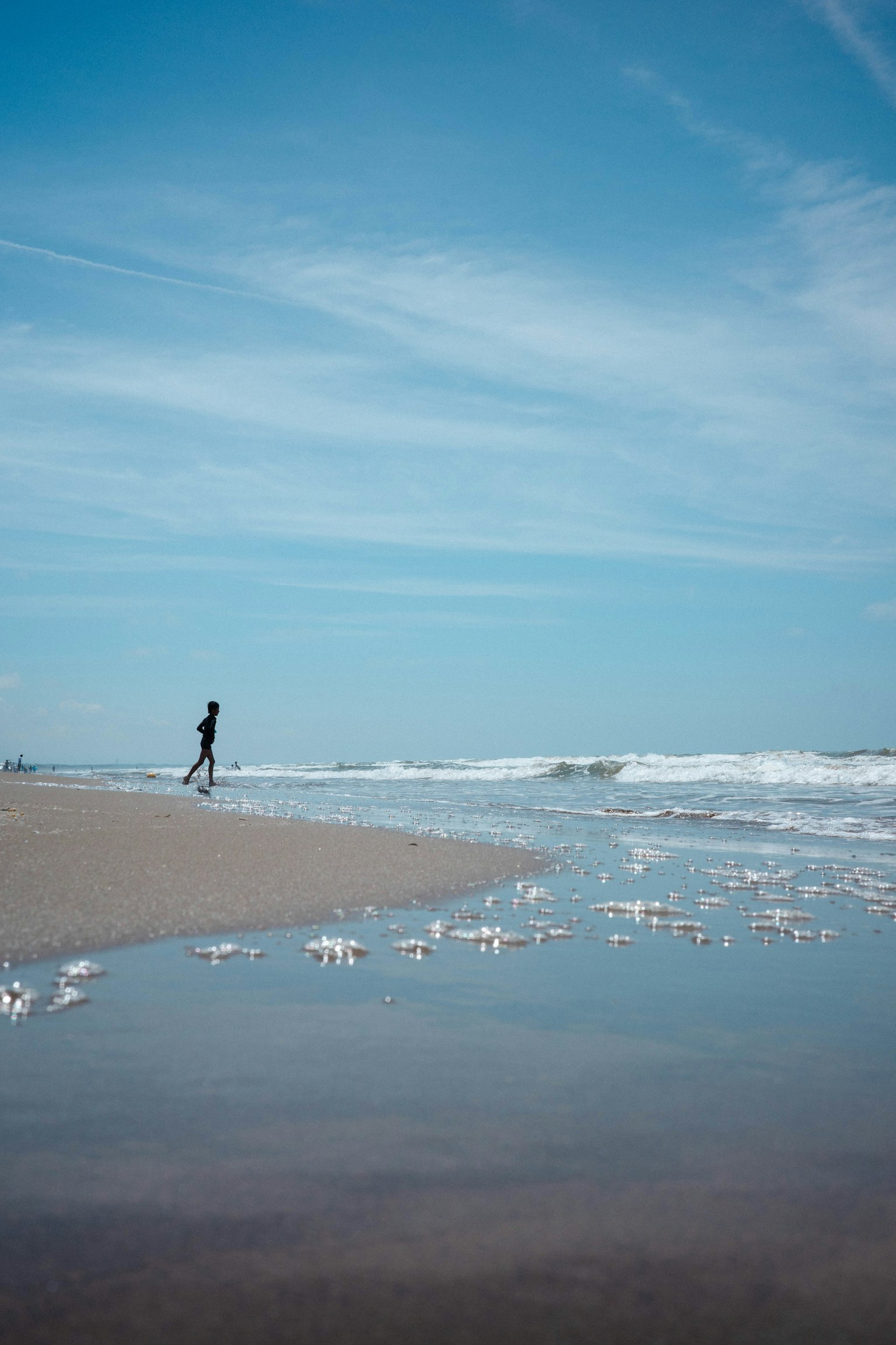 Silhouette di una persona che cammina lungo una spiaggia sotto un cielo blu