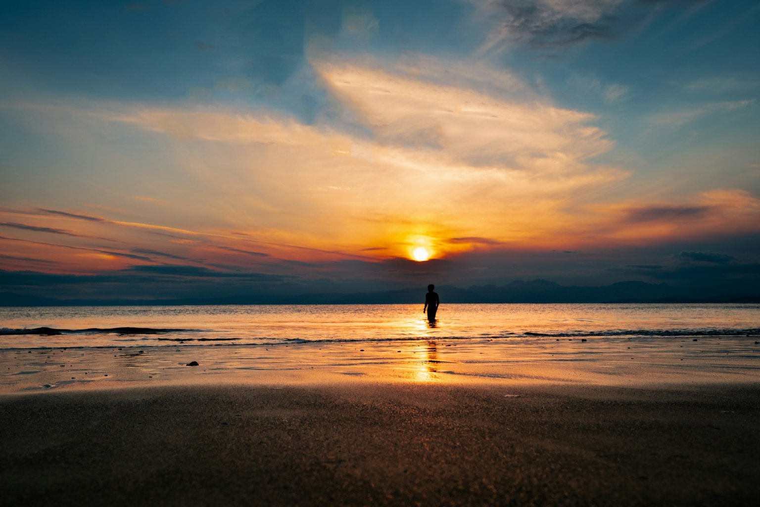 夕阳下站在海滩上的人物轮廓与天空的鲜艳色彩