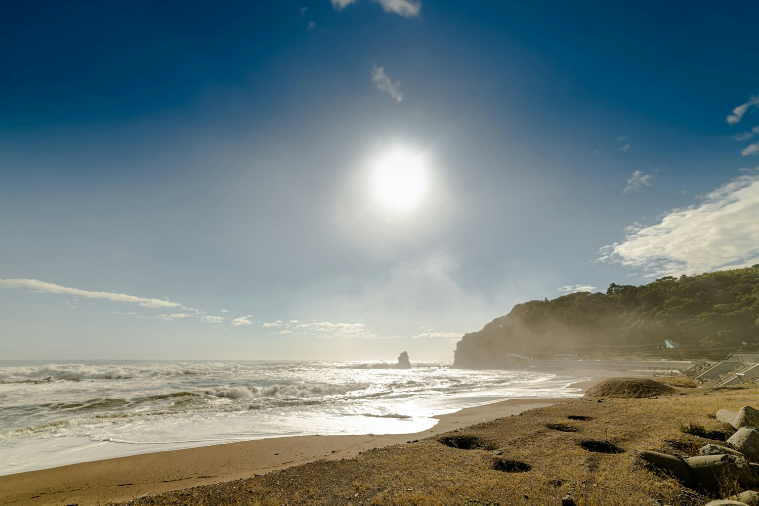Coastal landscape with blue sky and bright sun waves crashing on sandy beach