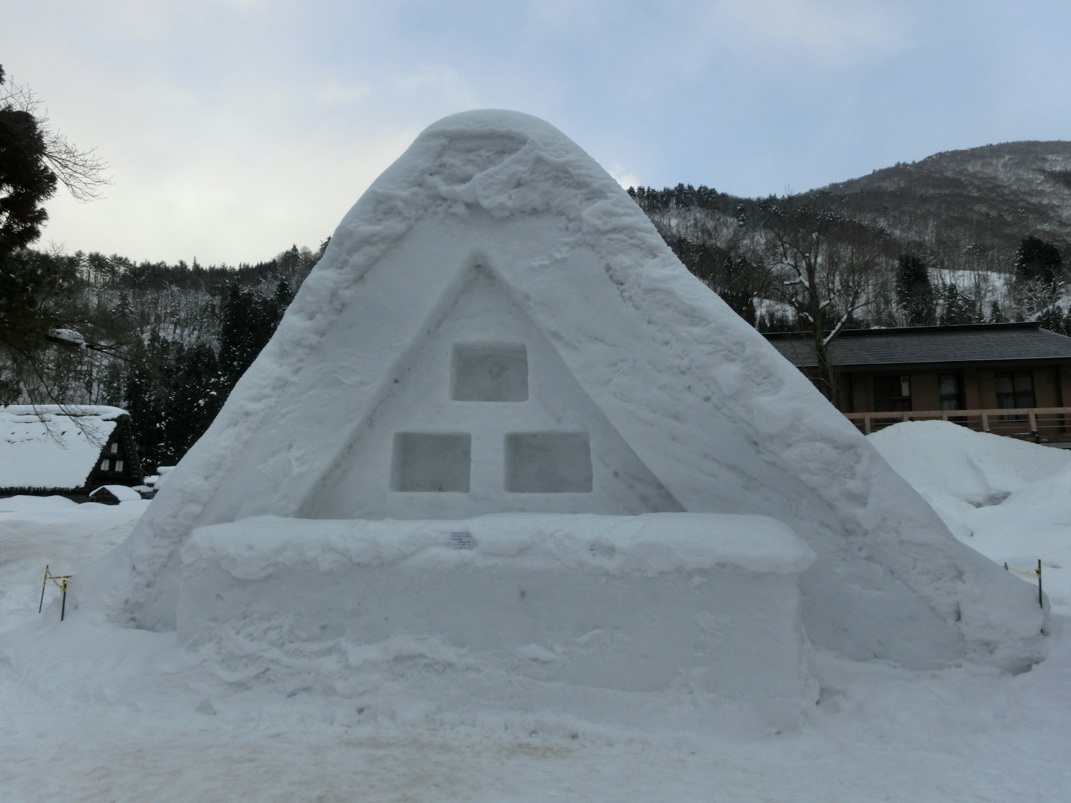 Scultura di neve di una capanna triangolare circondata da un paesaggio innevato