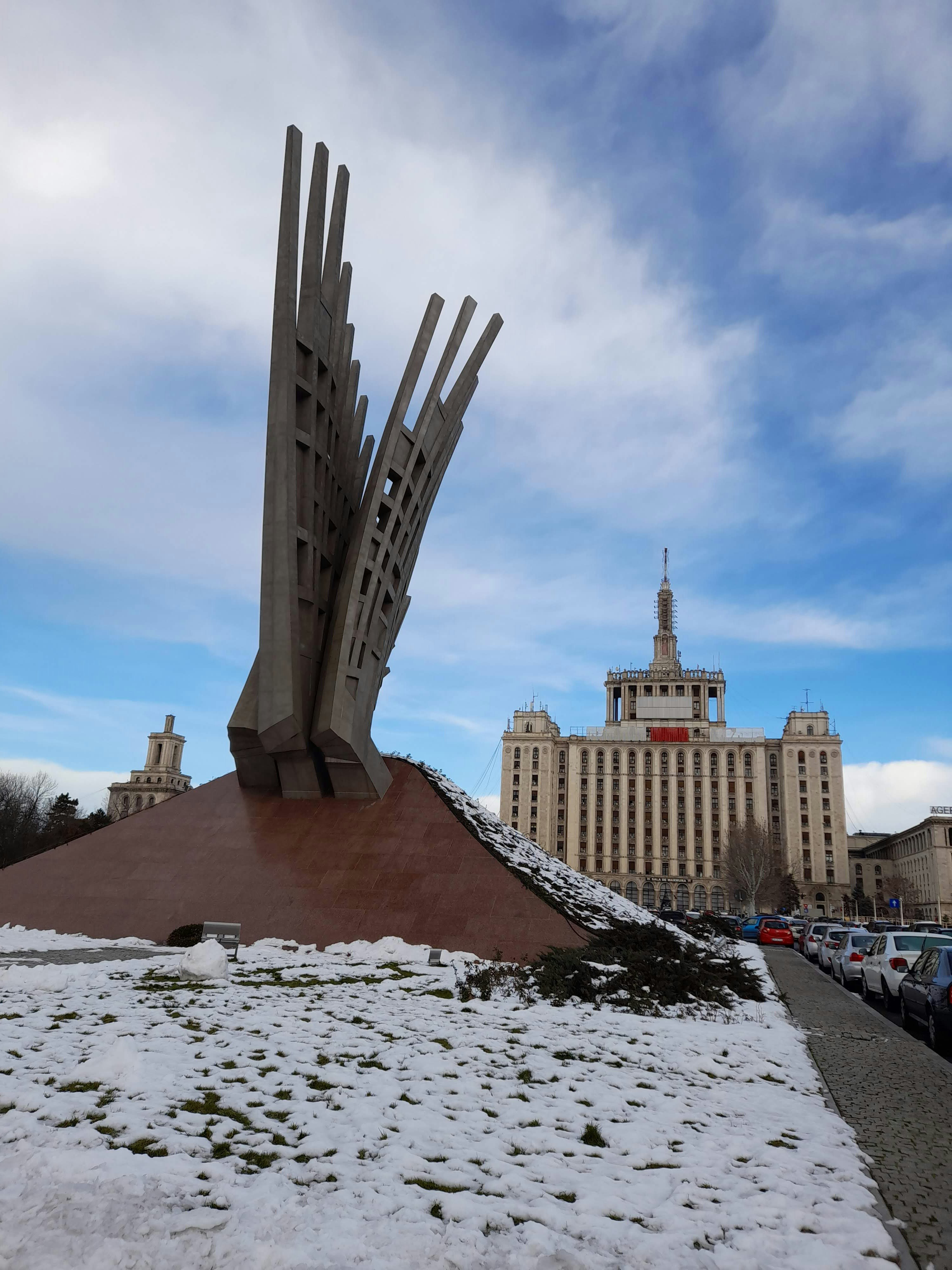 Snowy plaza walkway with a monument and distant high-rise buildings