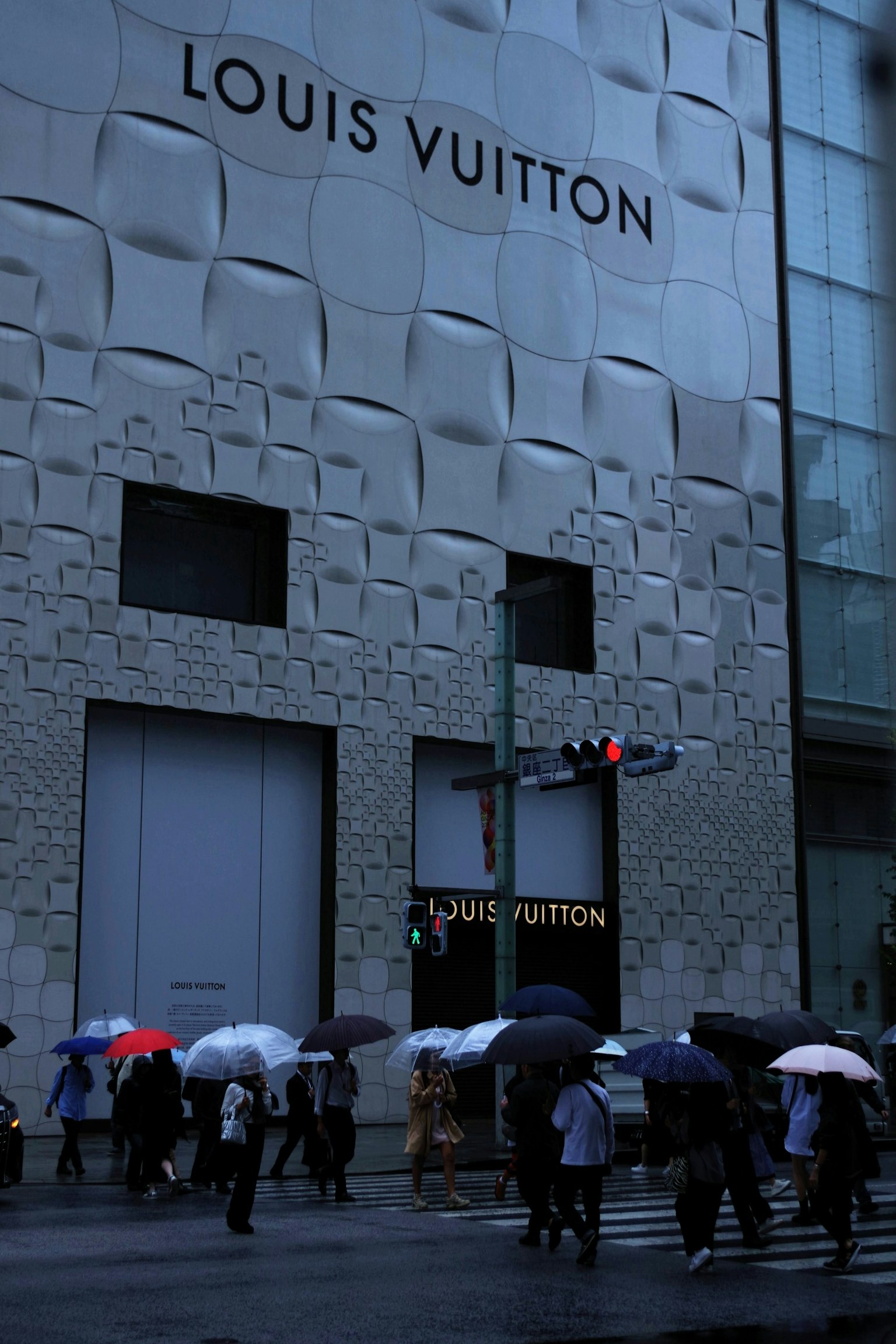 Des personnes avec des parapluies marchant dans la rue devant un magasin Louis Vuitton