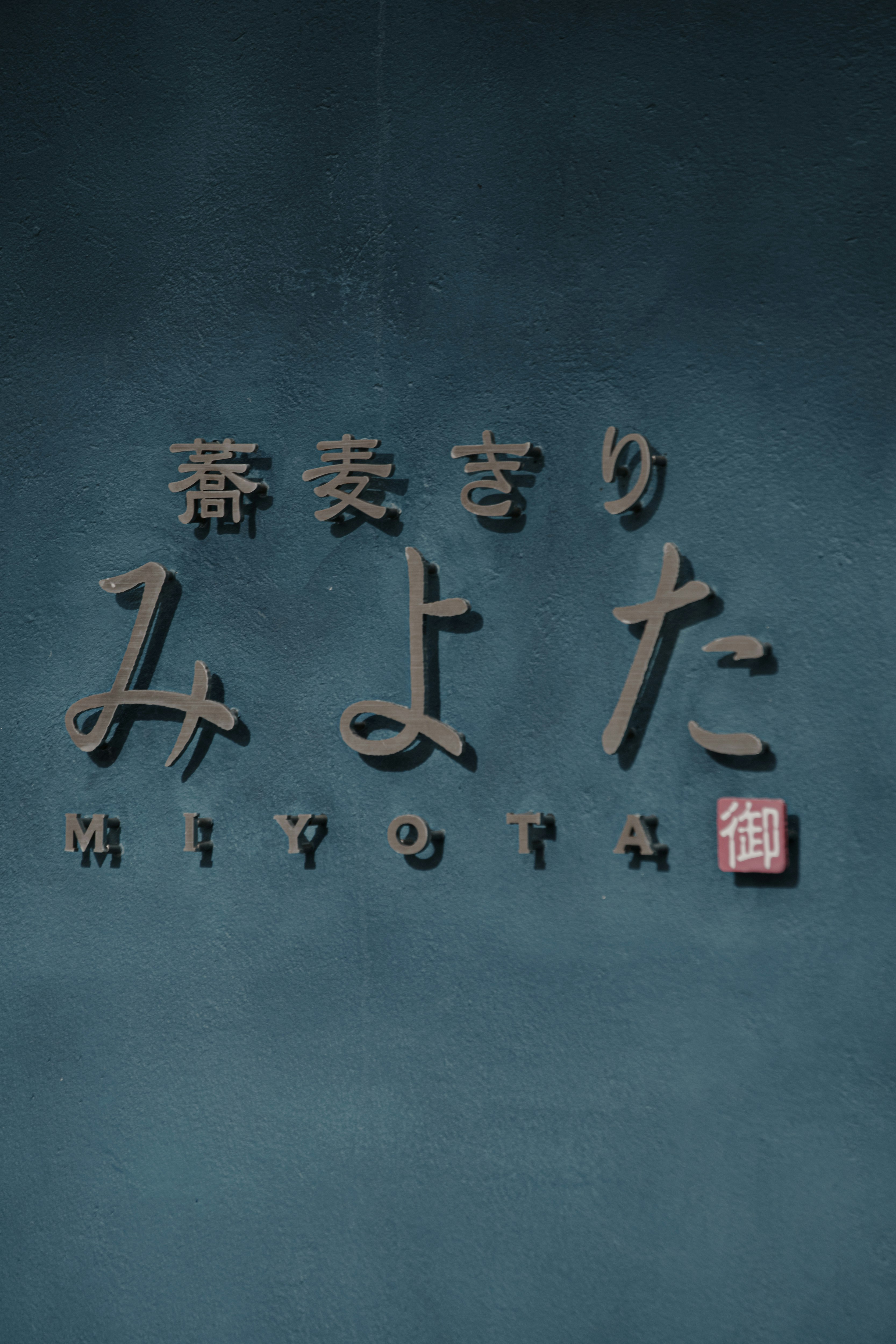 青い壁に刻まれた文字と小さな木札のある看板