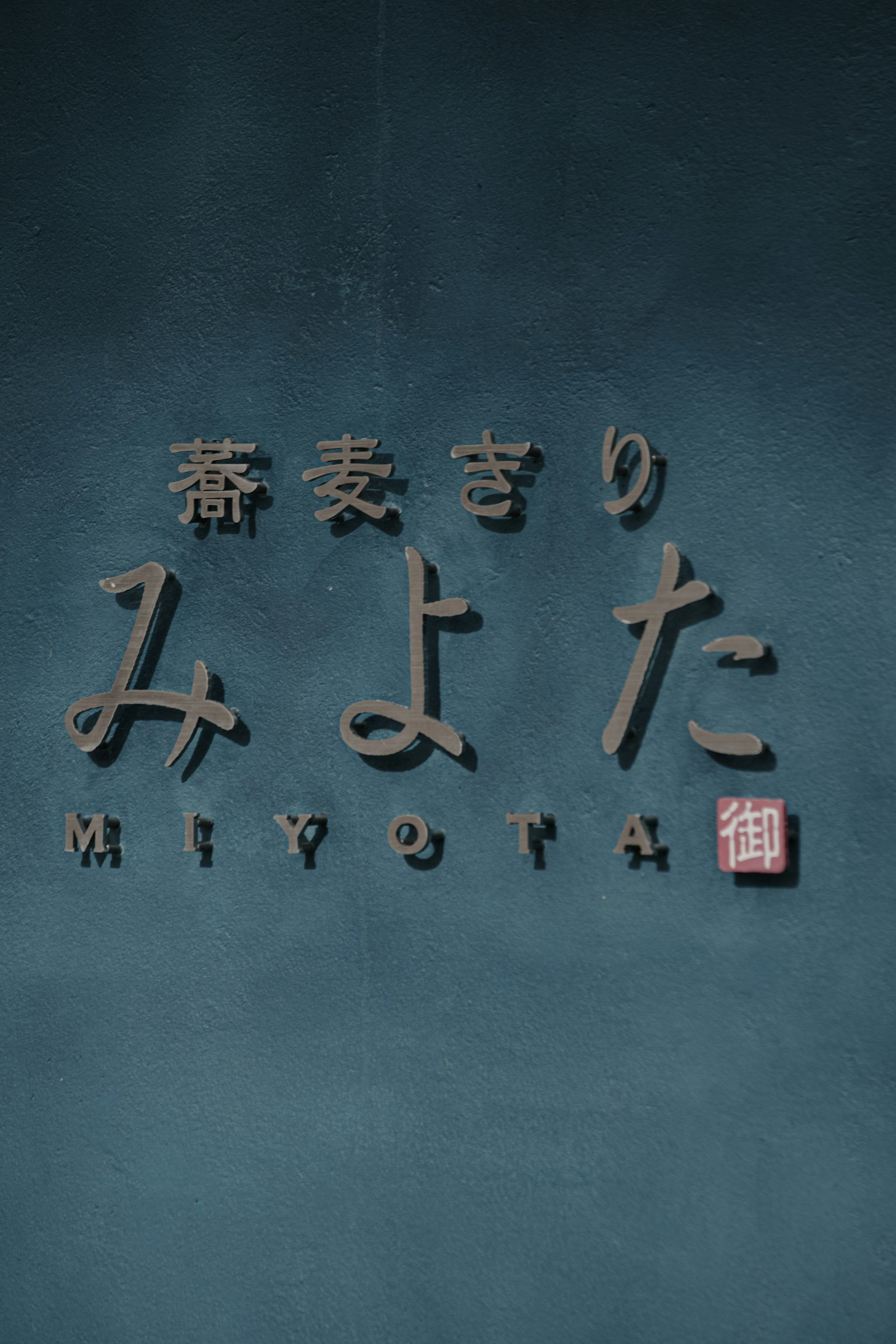 3D-Schild mit dem Namen Miyota an einer blauen Wand