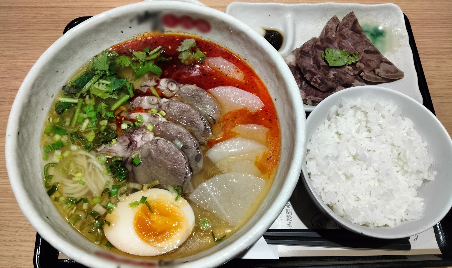 美味的拉面碗，上面放有切片肉和煮鸡蛋，旁边配有米饭和肉菜