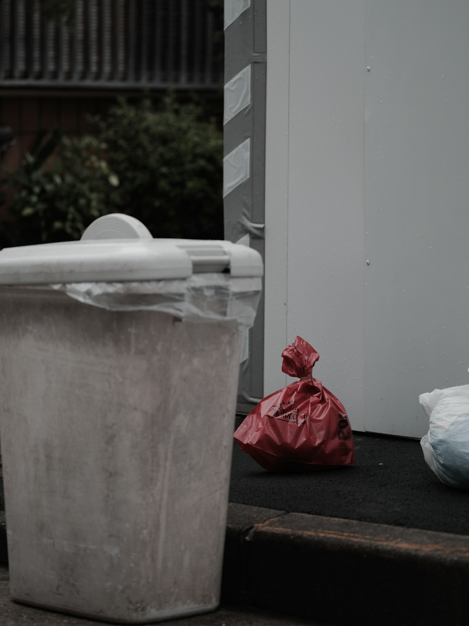 A white trash bin with red and blue trash bags nearby