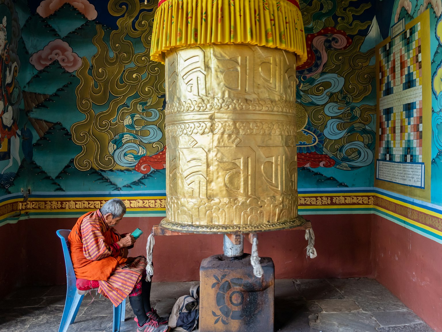 พระนั่งอยู่ข้างล้อสวดมนต์ทองขนาดใหญ่ในวัดที่มีสีสัน