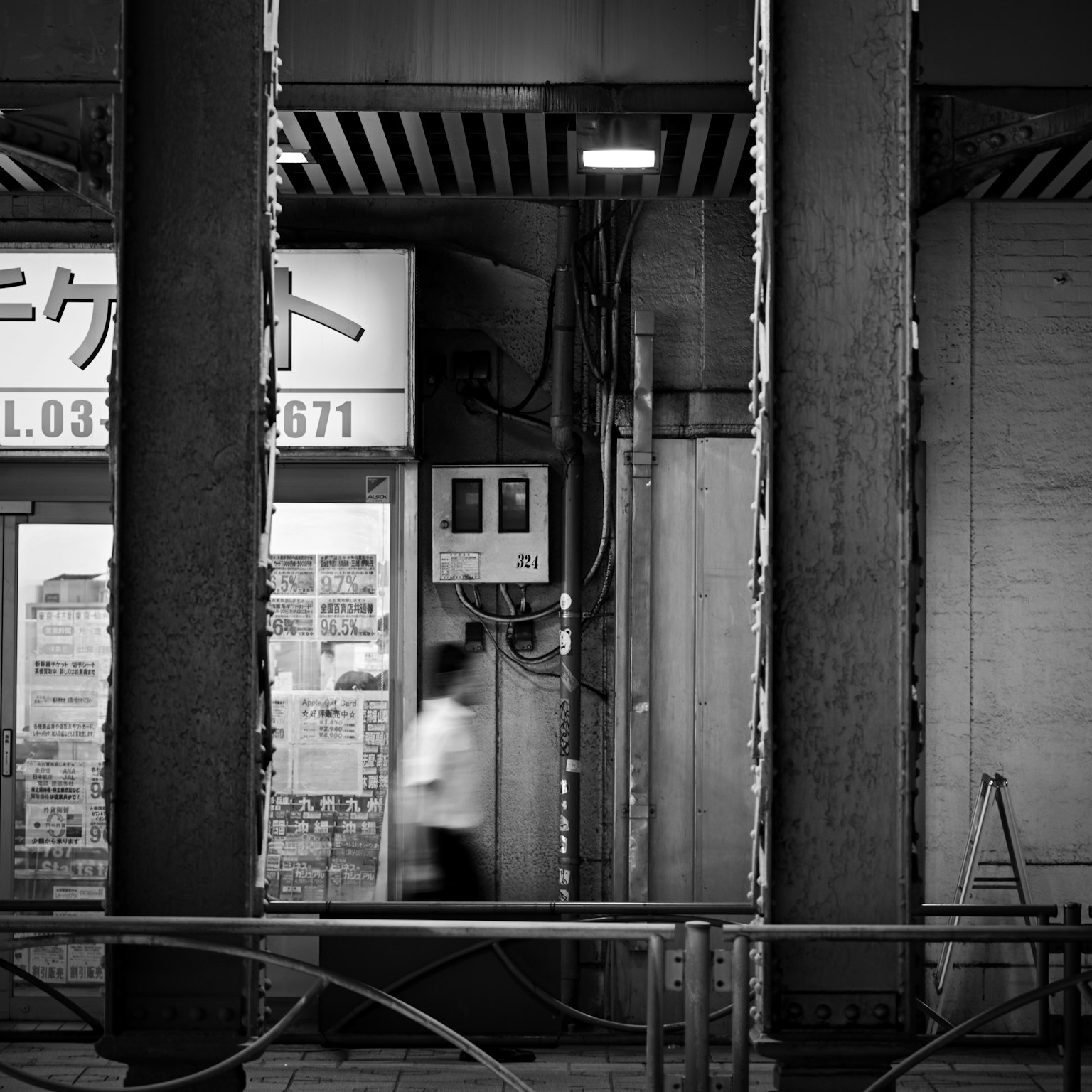 Black and white urban scene with a person walking by visible lighting and electrical box