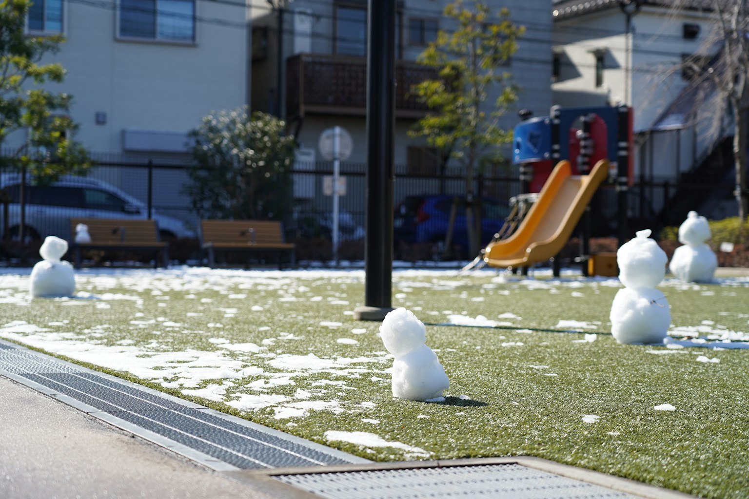 Several snowmen on a grassy area in a park with a slide