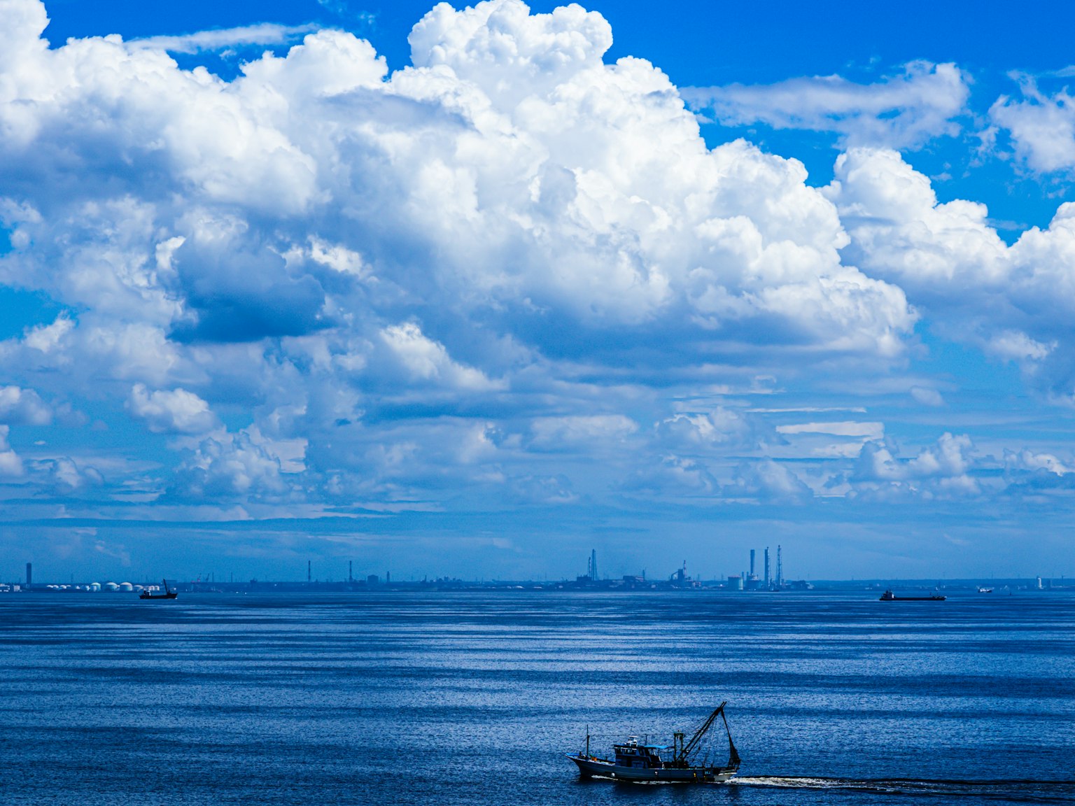A fishing boat floats on a blue sea under a sky filled with white clouds