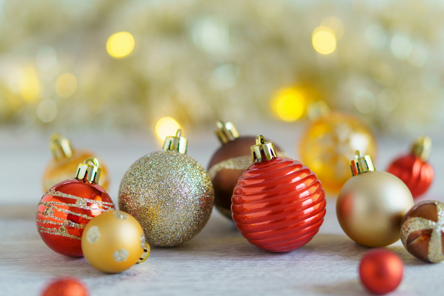 Una collezione di ornamenti natalizi colorati in rosso e oro sparsi su una superficie di legno con luci bokeh morbide sullo sfondo