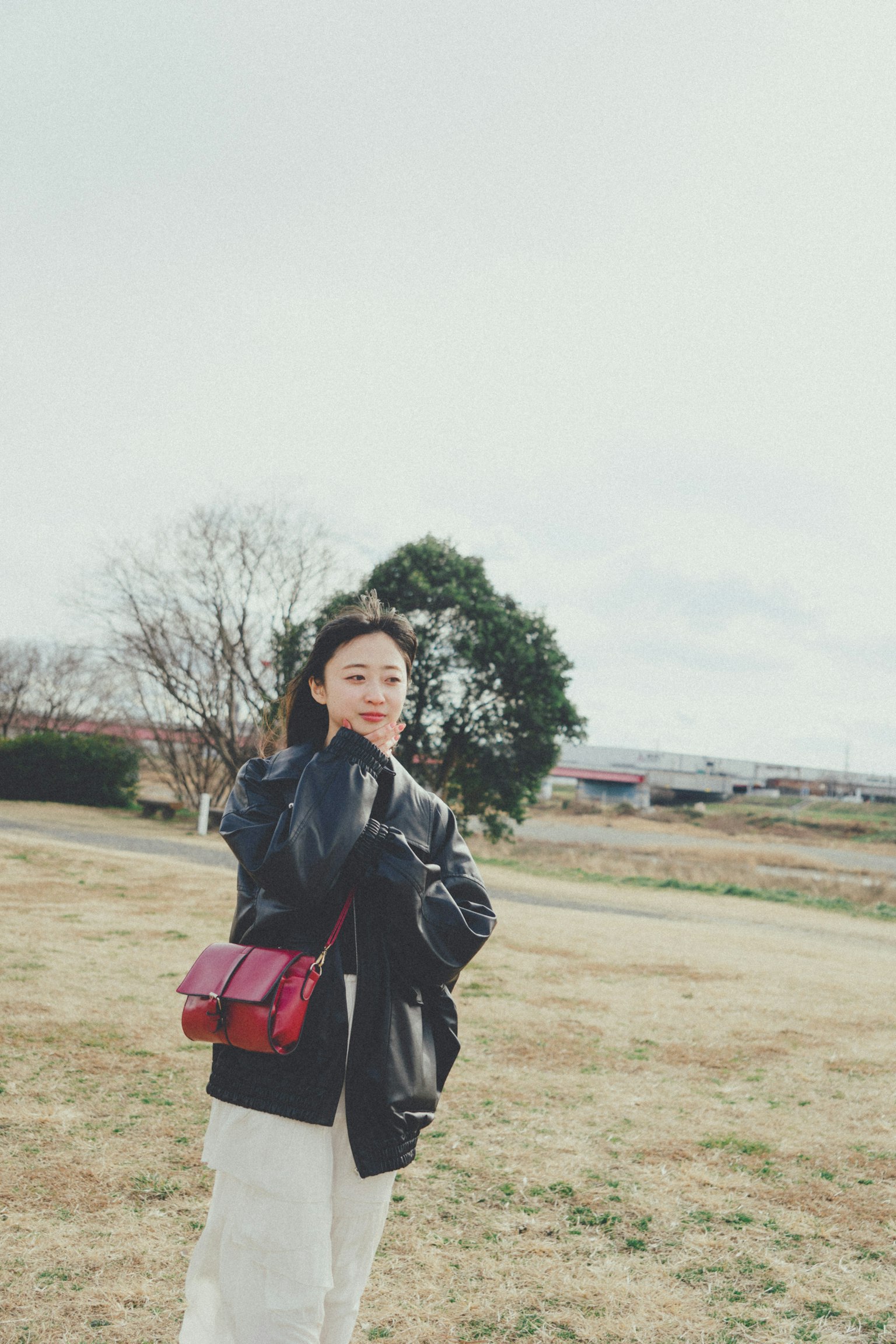 一位穿着黑色夹克，手持红色包包在公园微笑的女性