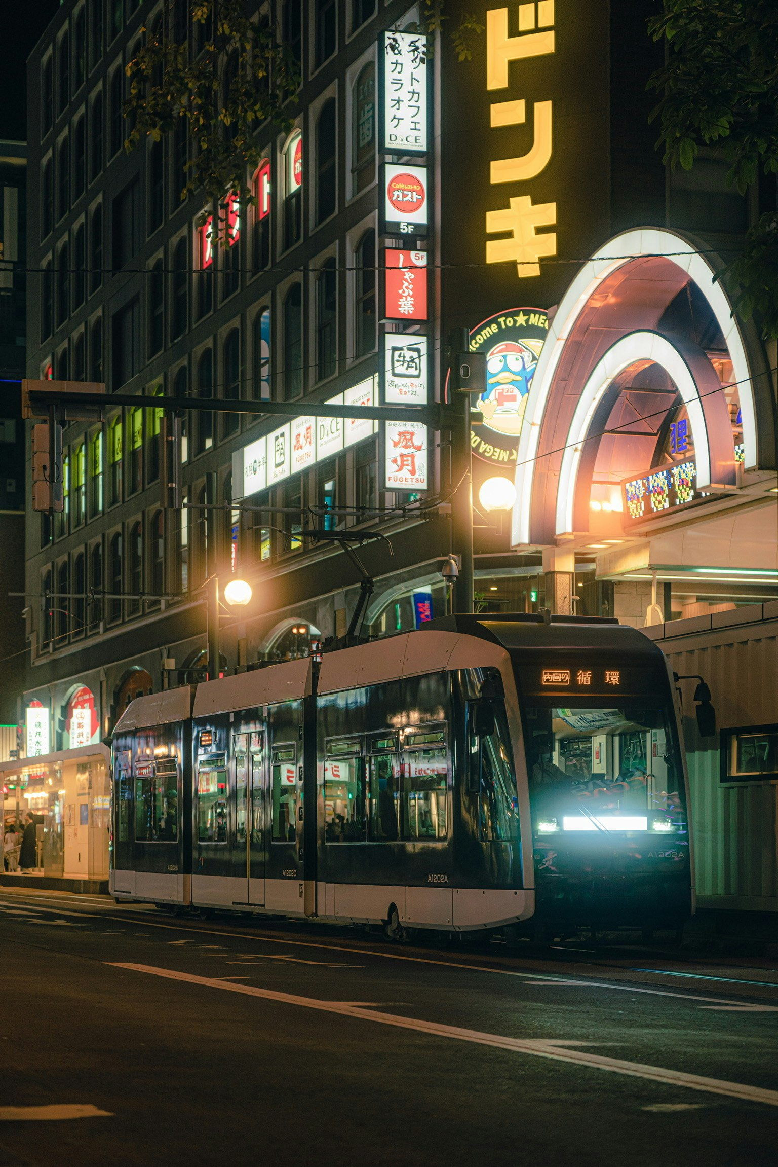 Tram in a city street at night with colorful signs