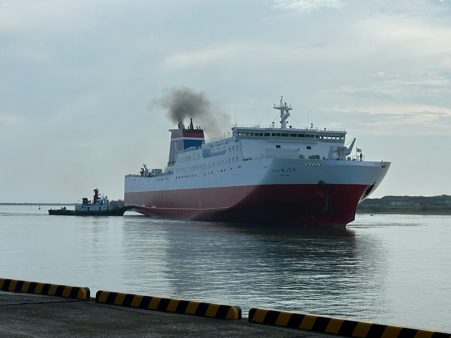 Large ferry docked at the port featuring red and white colors emitting smoke