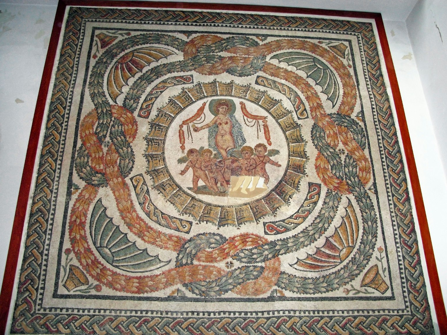 Mosaik ini menggambarkan adegan mitologis kuno dengan sosok yang berkumpul di tengah