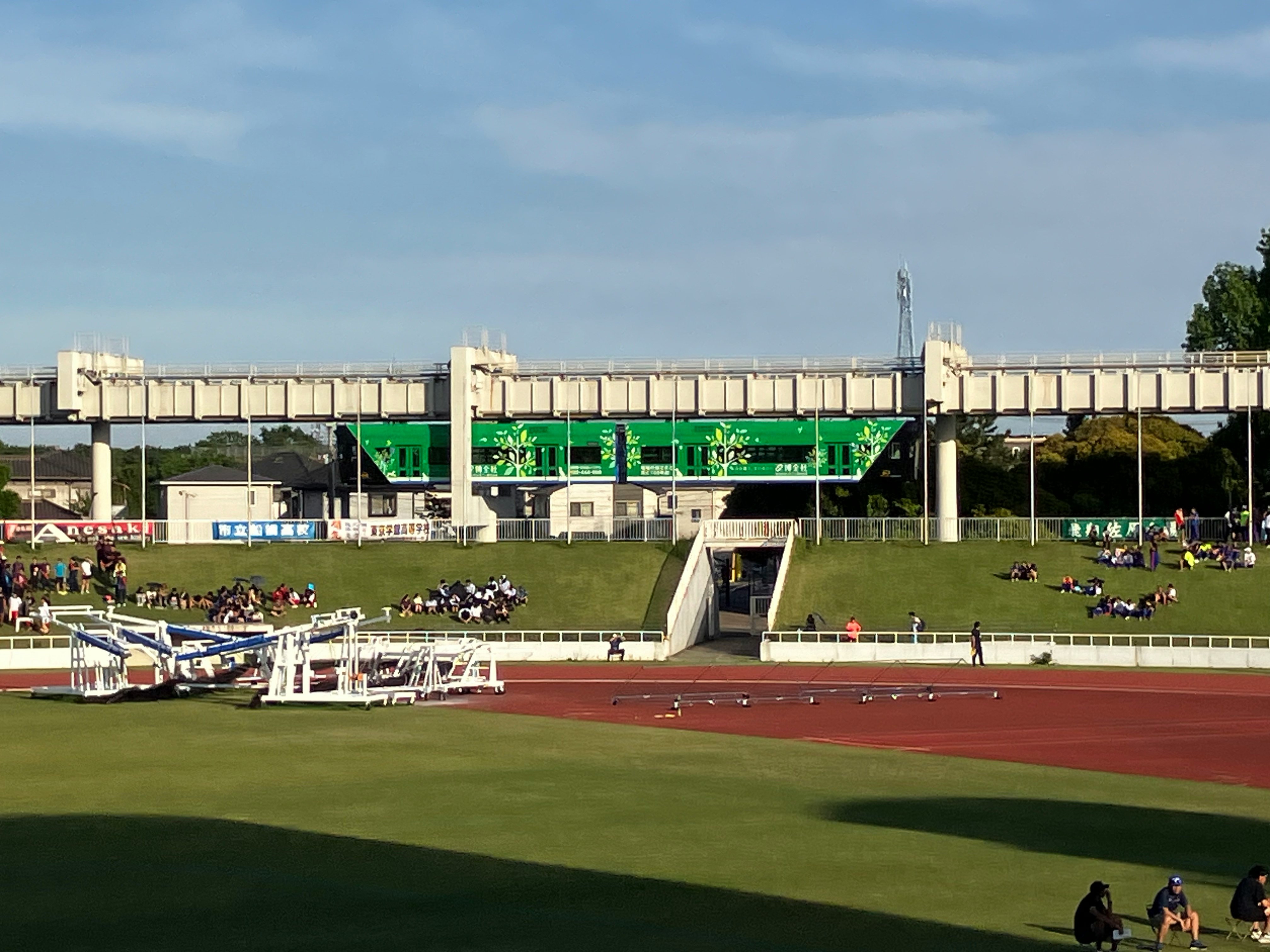 Estadio de atletismo con gradas y pista, monorraíl verde pasando