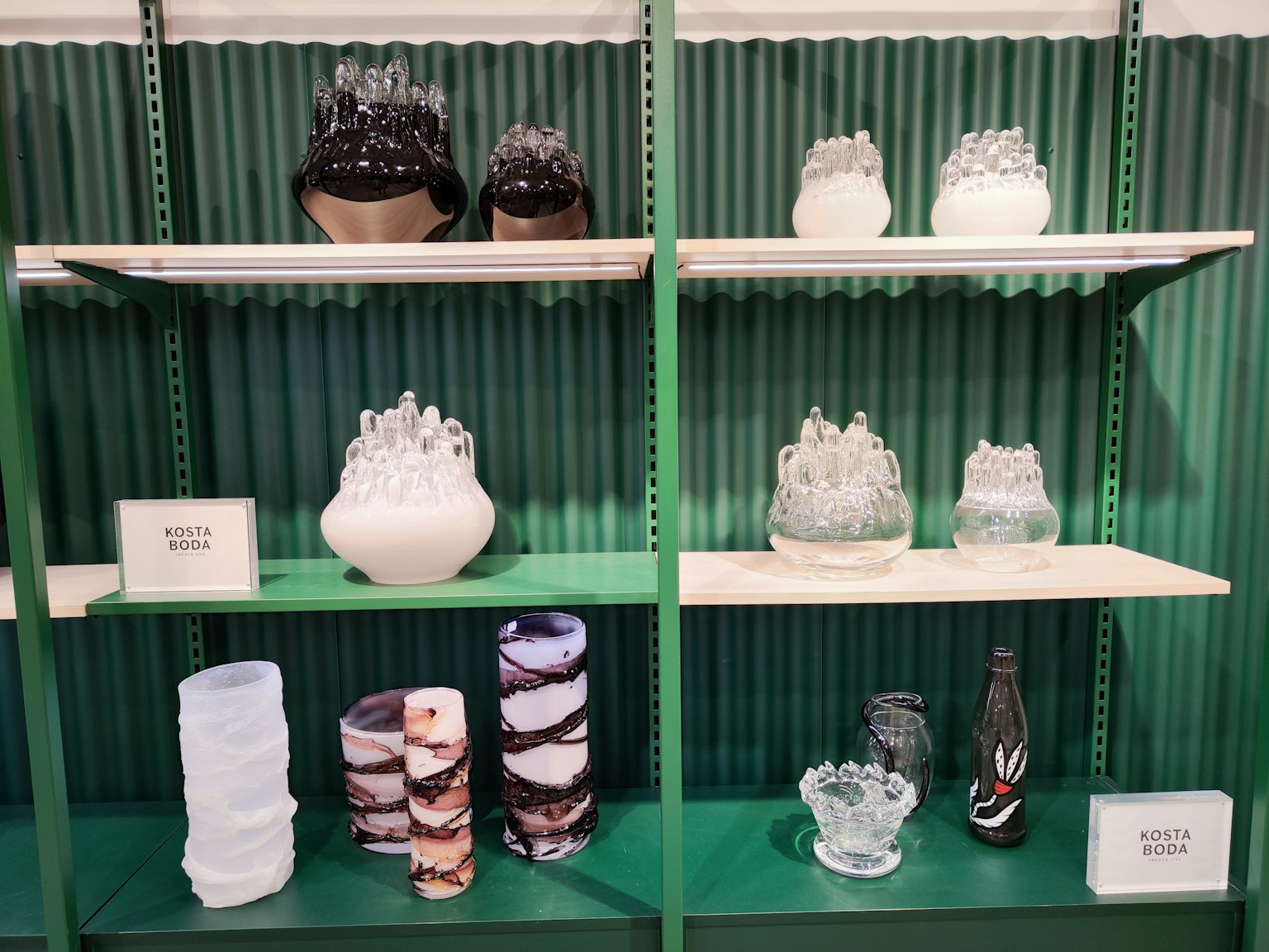 Verschiedene Glasartikel auf grünen Regalen ausgestellt