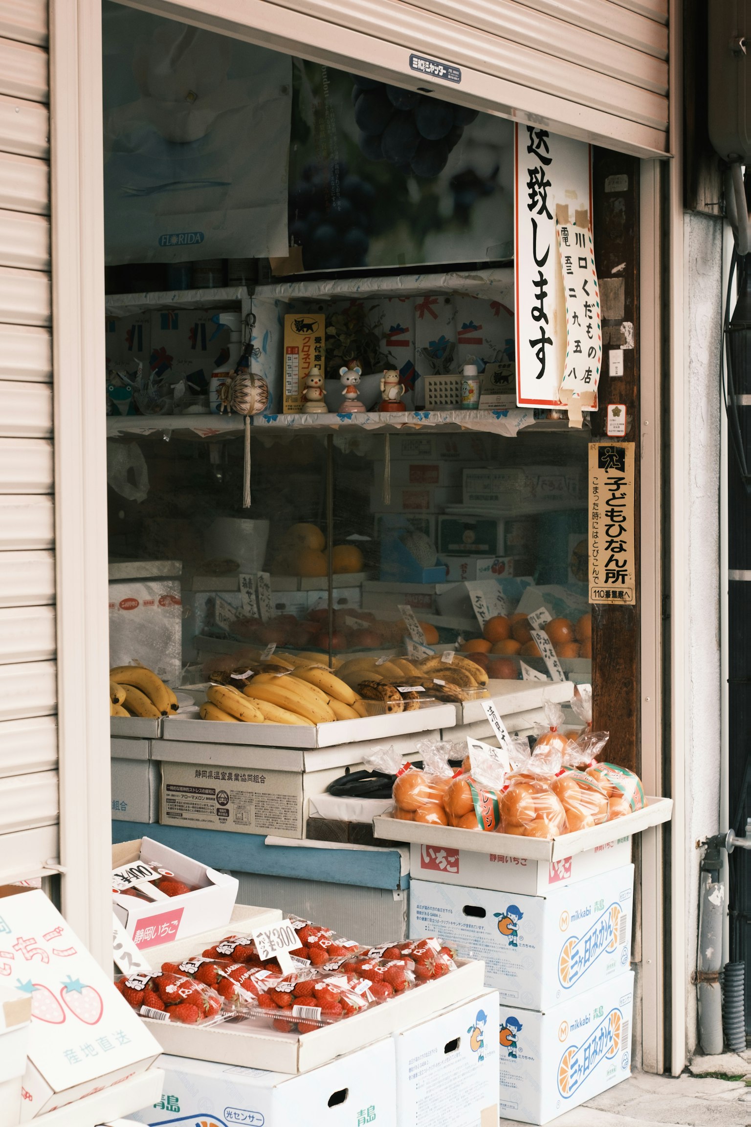 Exterior de una pequeña tienda que exhibe frutas y verduras frescas con señalización en japonés