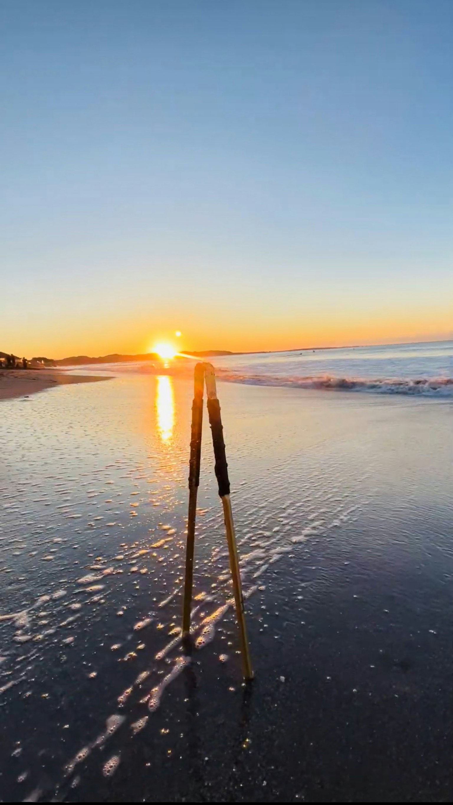Pemandangan matahari terbenam yang indah memantul di pantai dengan tripod di latar depan