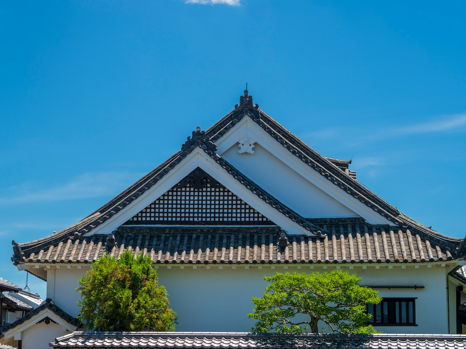 Traditional Japanese building roof under a clear blue sky with green trees