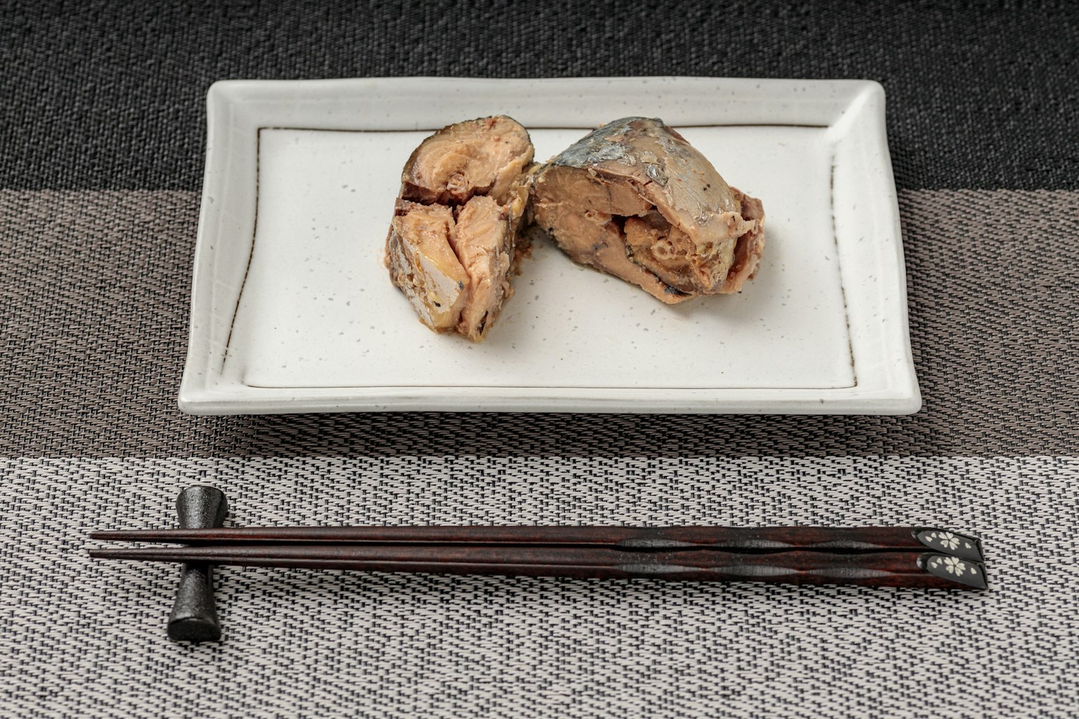 白色盤子上的兩塊魚和附近的黑色筷子