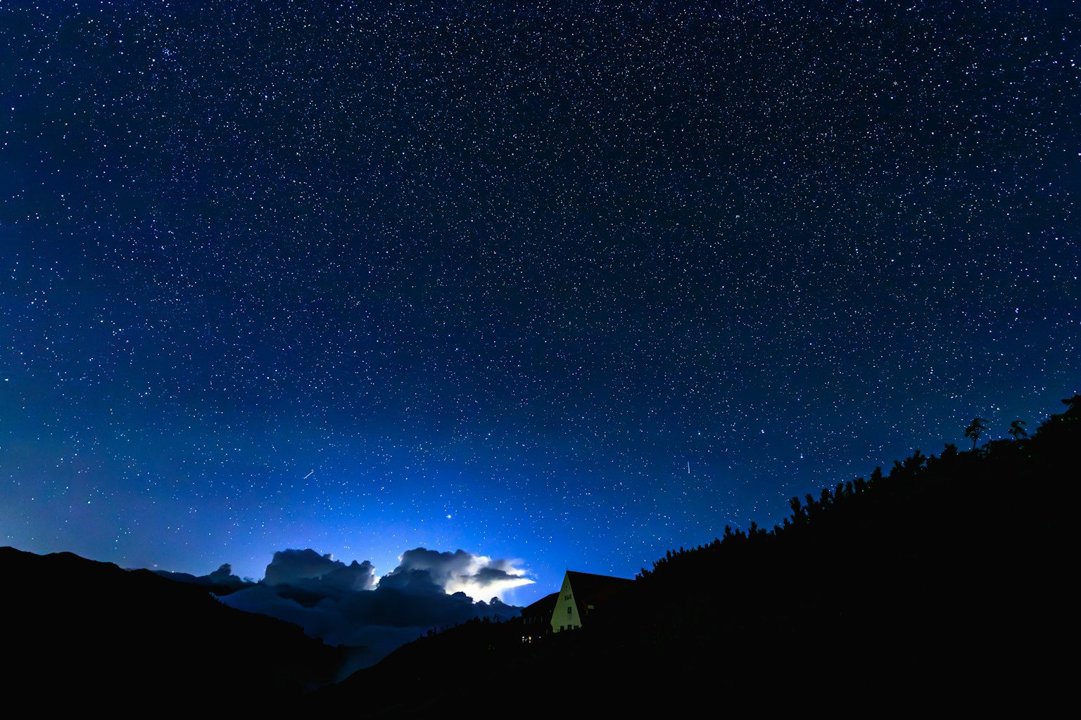 Cielo notturno pieno di stelle con montagne in silhouette in primo piano
