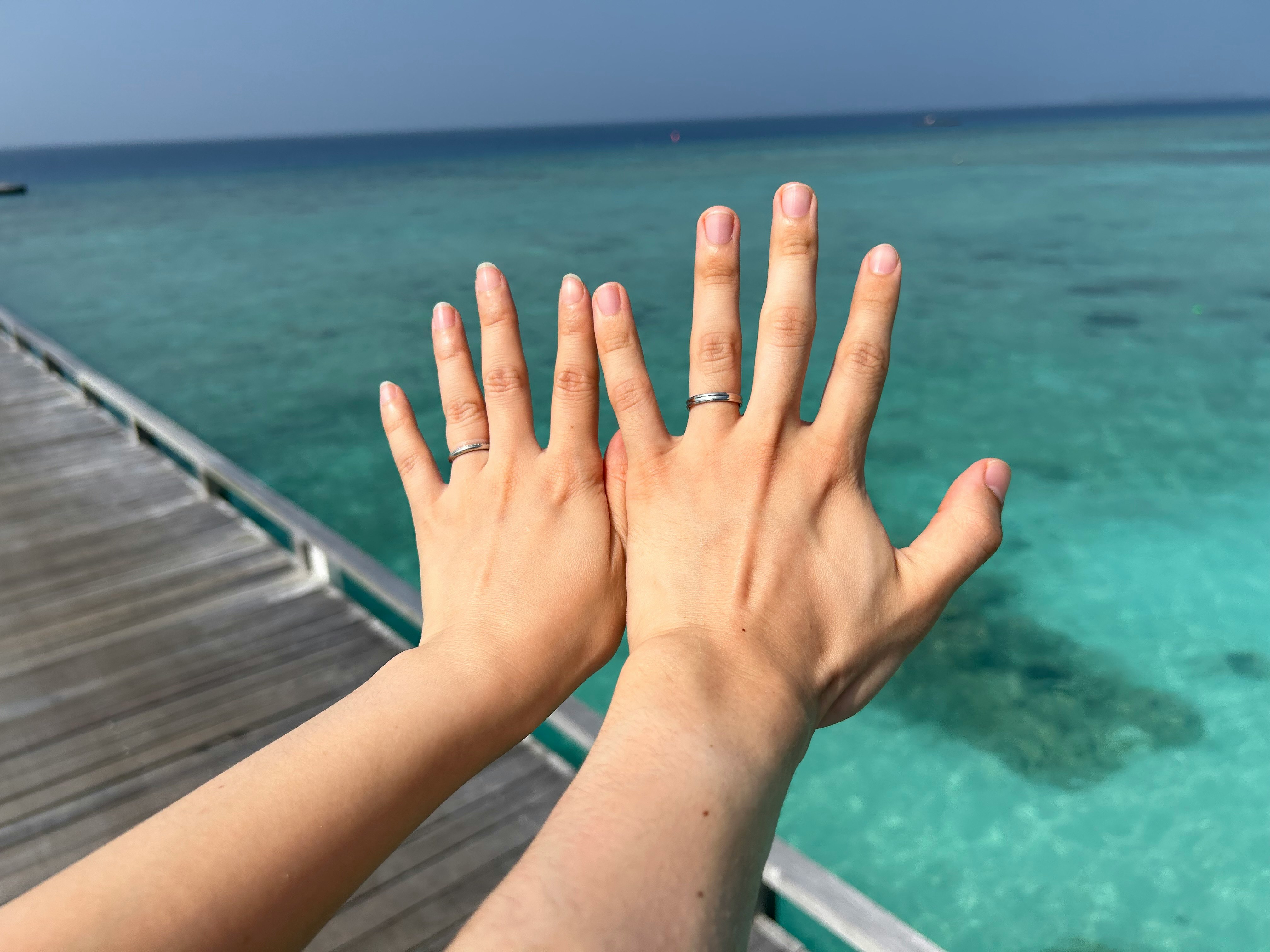 海辺の桟橋で手を重ねる指輪のハネムーンの雰囲気