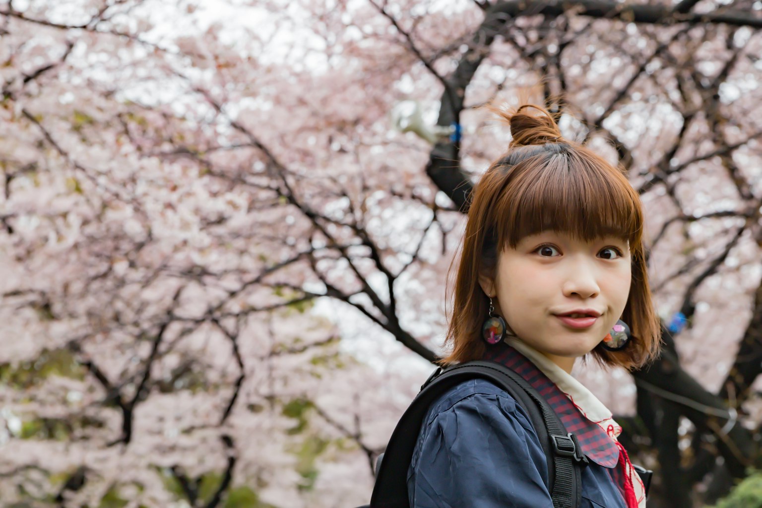 Ritratto di una ragazza davanti a alberi di ciliegio in fiore con i capelli raccolti e fiori rosa sullo sfondo