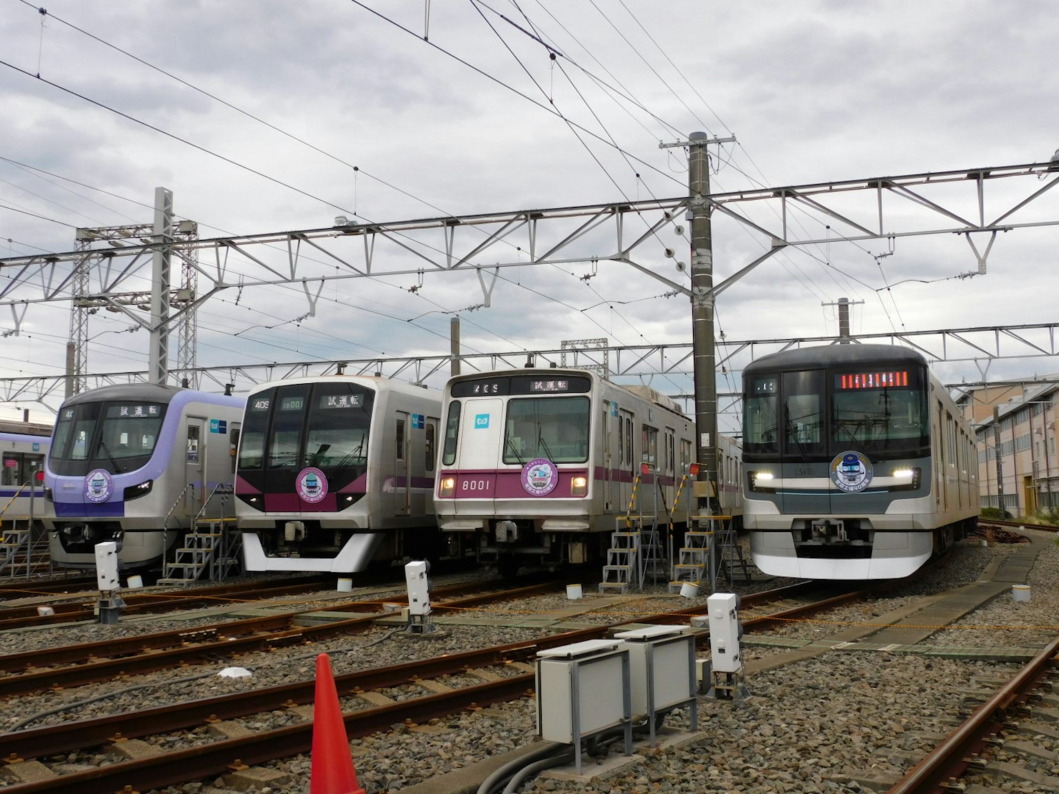 ภาพของรถไฟหลายขบวนเรียงกันบนรางรถไฟท่ามกลางท้องฟ้าที่มีเมฆและสายไฟเหนือศีรษะ