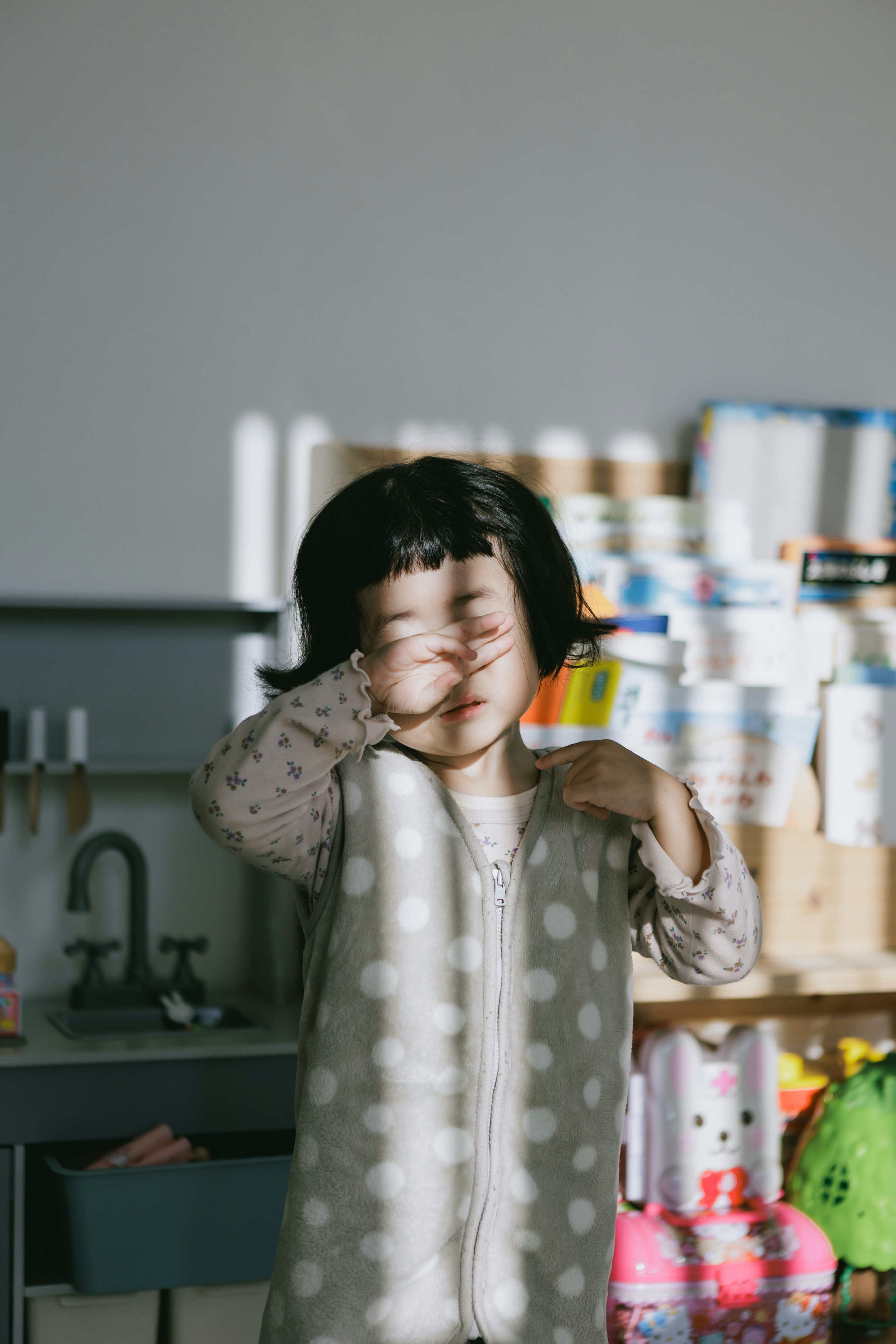 キッチンで手を耳に当てて眠そうにする子ども