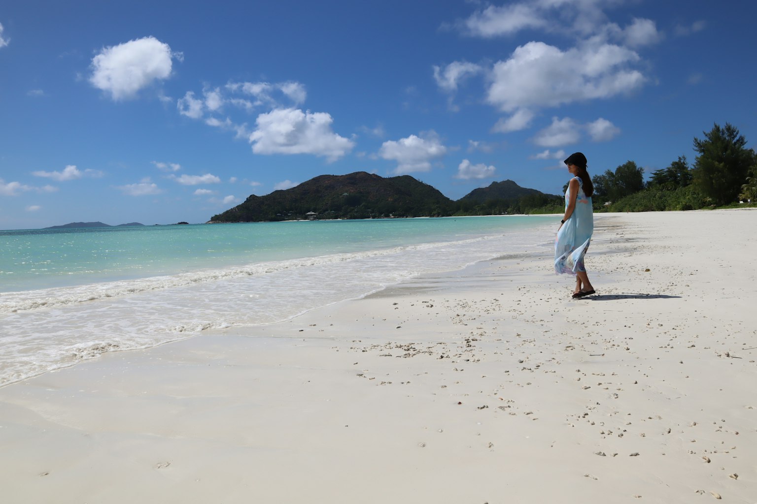 Femme marchant sur une plage de sable blanc avec océan bleu et nuages