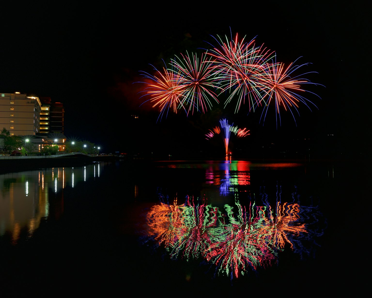 Espectáculo de fuegos artificiales coloridos en el cielo nocturno con reflejos en la superficie del agua