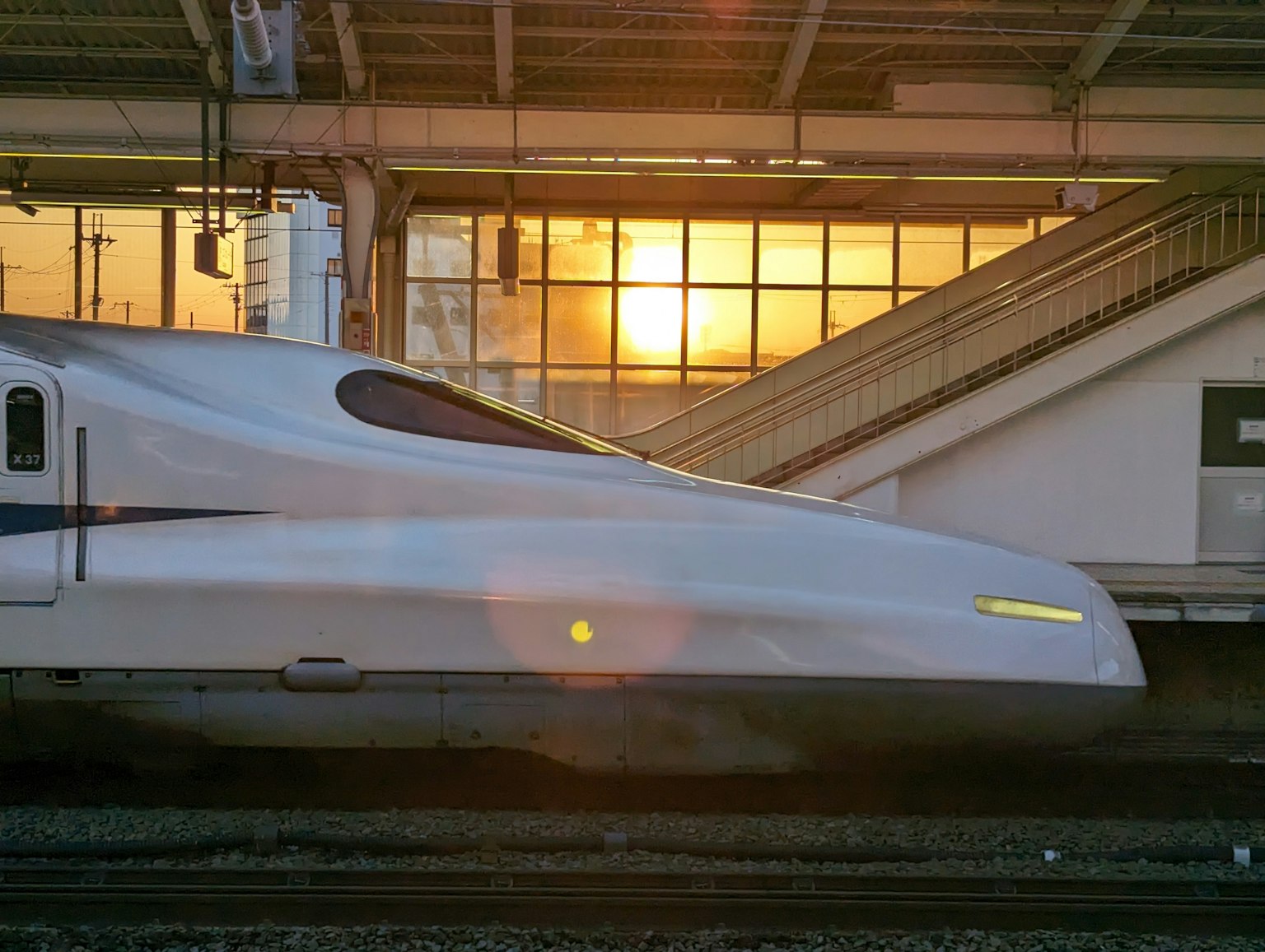 Tampilan samping Shinkansen di stasiun dengan latar belakang matahari terbenam