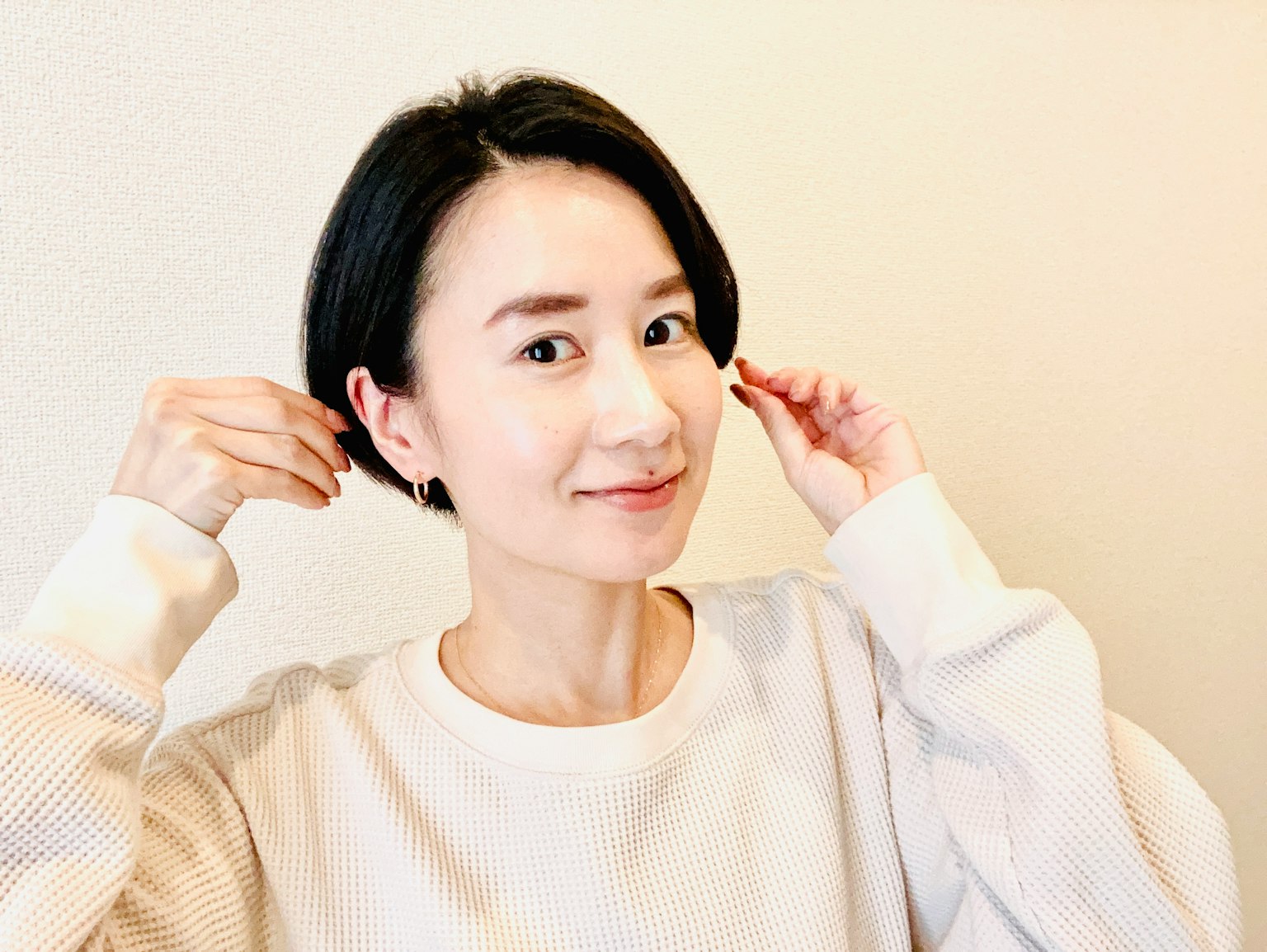 穿著白色毛衣的女性微笑著，留著短黑髮
