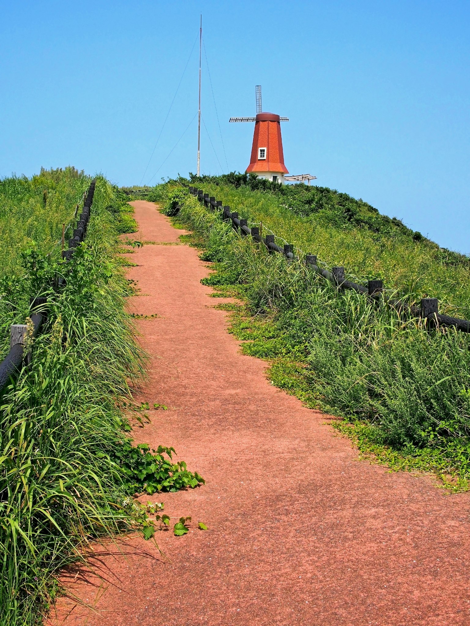 A dirt path leading to a windmill surrounded by green grass
